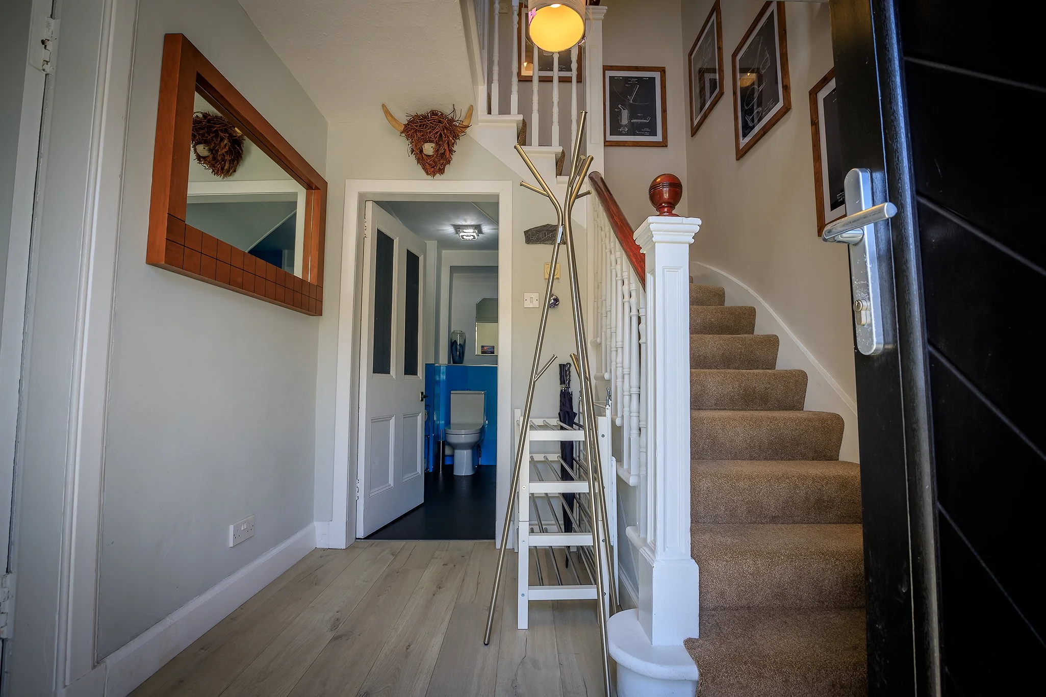 Entrance area with stairs, mirror, decorative animal head wall hangings, and a view into a bathroom with blue walls and a toilet.