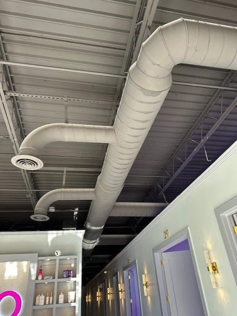Indoor ceiling with large white HVAC ductwork and vents, part of an industrial or commercial building interior.
