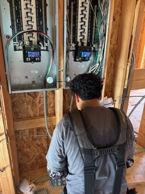 A person working on electrical panel wiring inside a wooden structure.