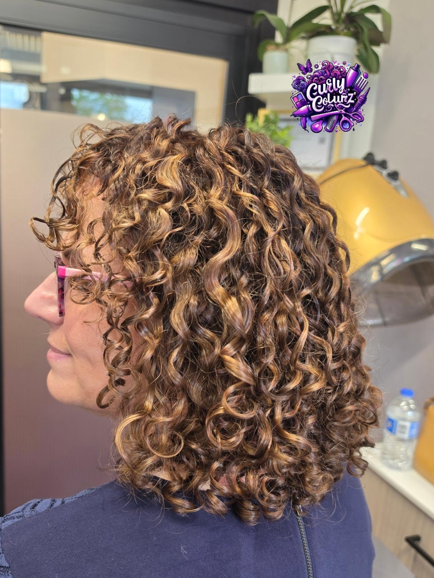 Hand-painted pintura highlights on curly hair shown from the back at Curly Colurz