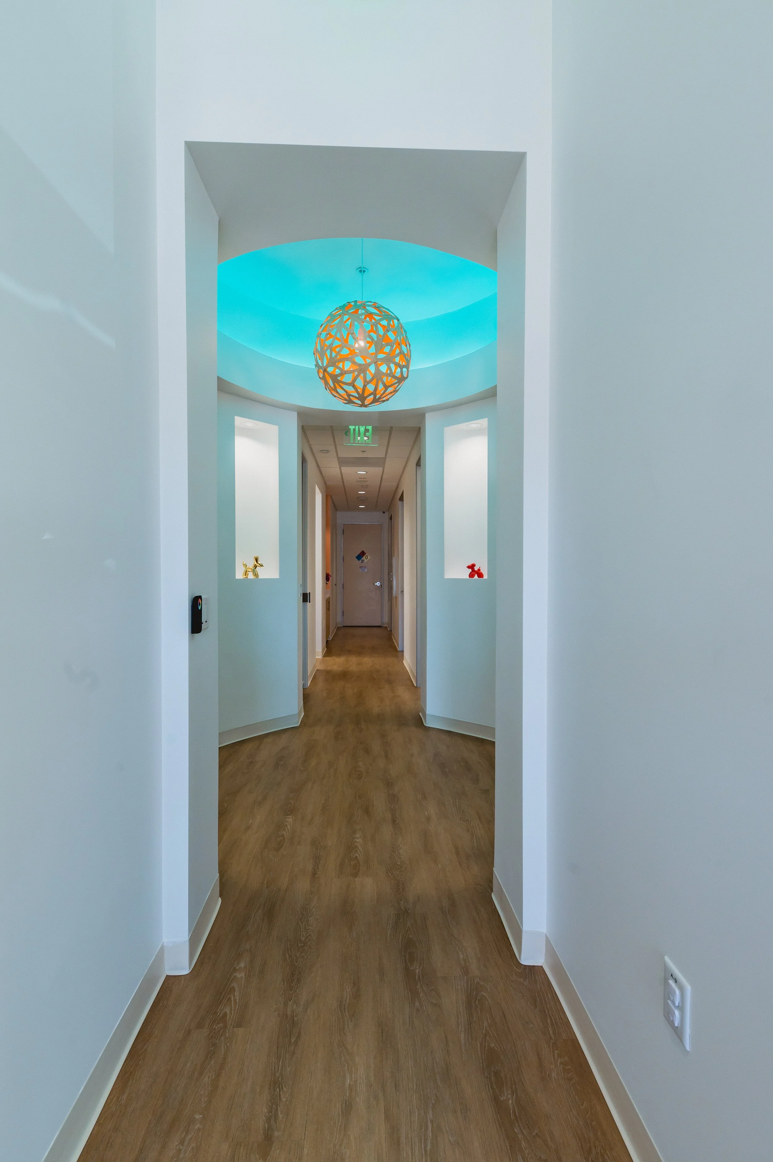 A hallway with light-colored walls, wooden flooring, and a decorative sphere-shaped pendant light hanging from a blue-lit ceiling.