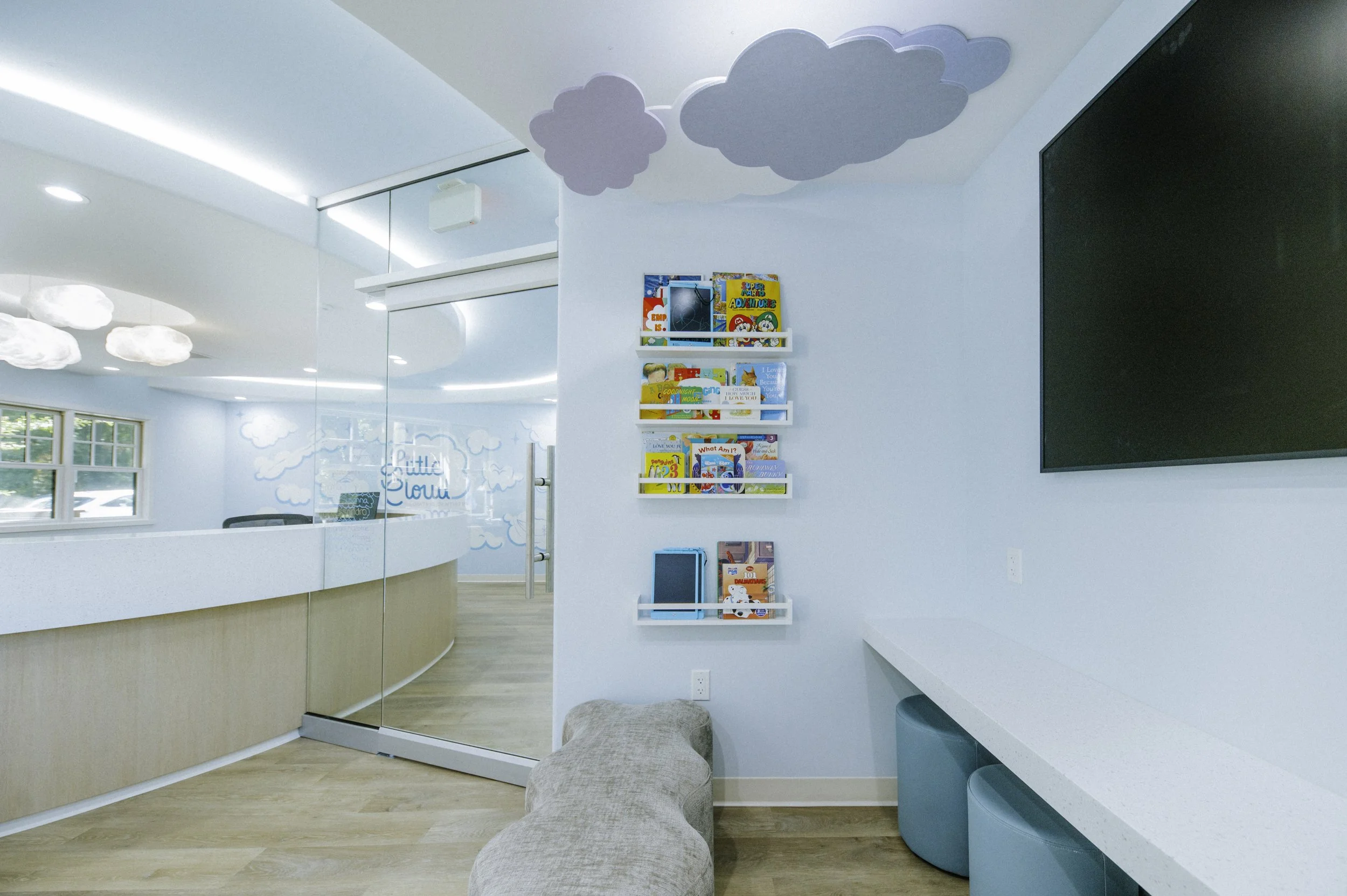Clouds made of felt add whimsy and help with acoustics. A wall hung desk provides space for coloring or homework. Kid sized ottomans provide seating.