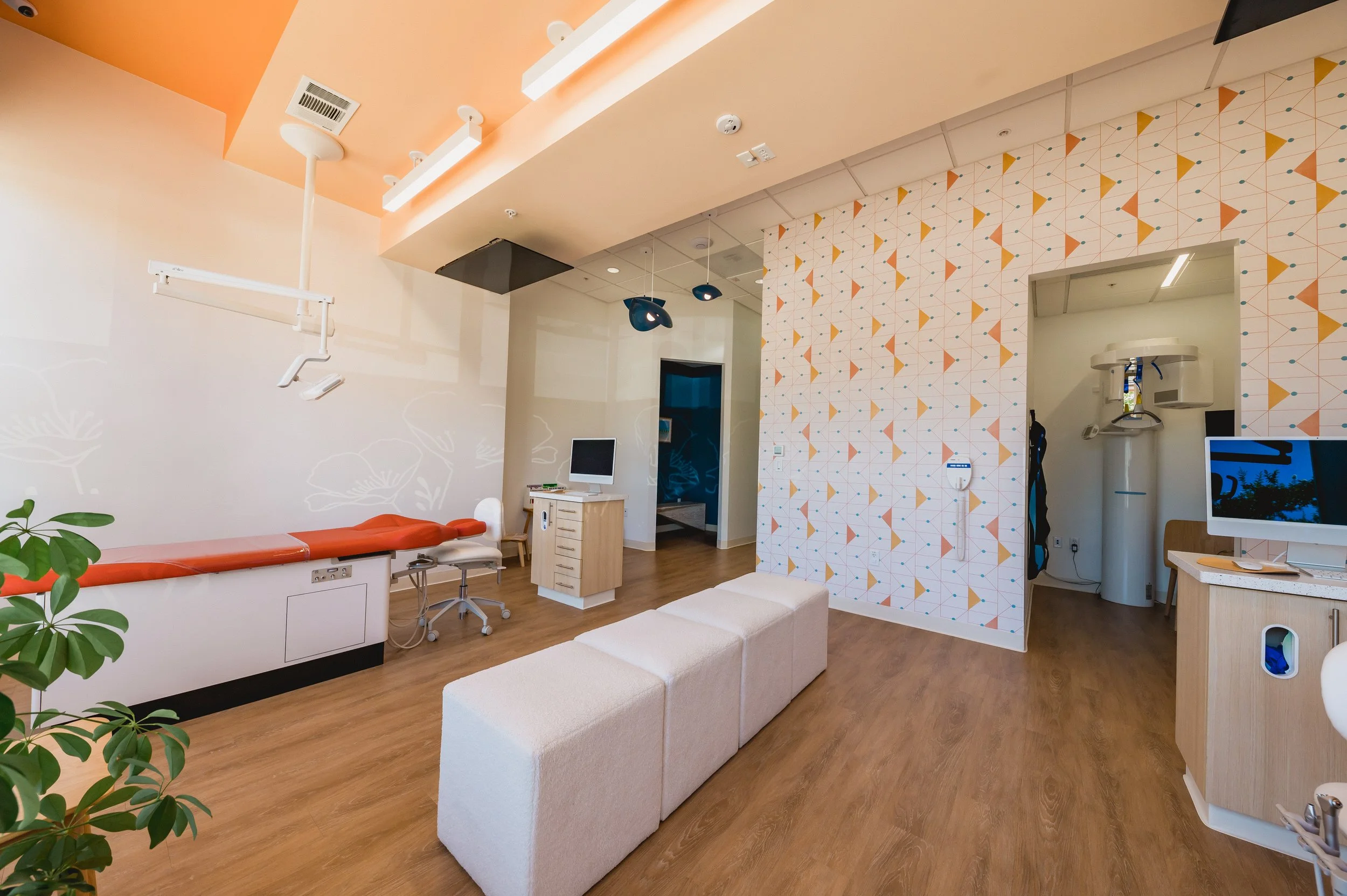 Modern dental clinic interior with dental chair, computer, and medical equipment, featuring wooden floors and colorful geometric wall decor.