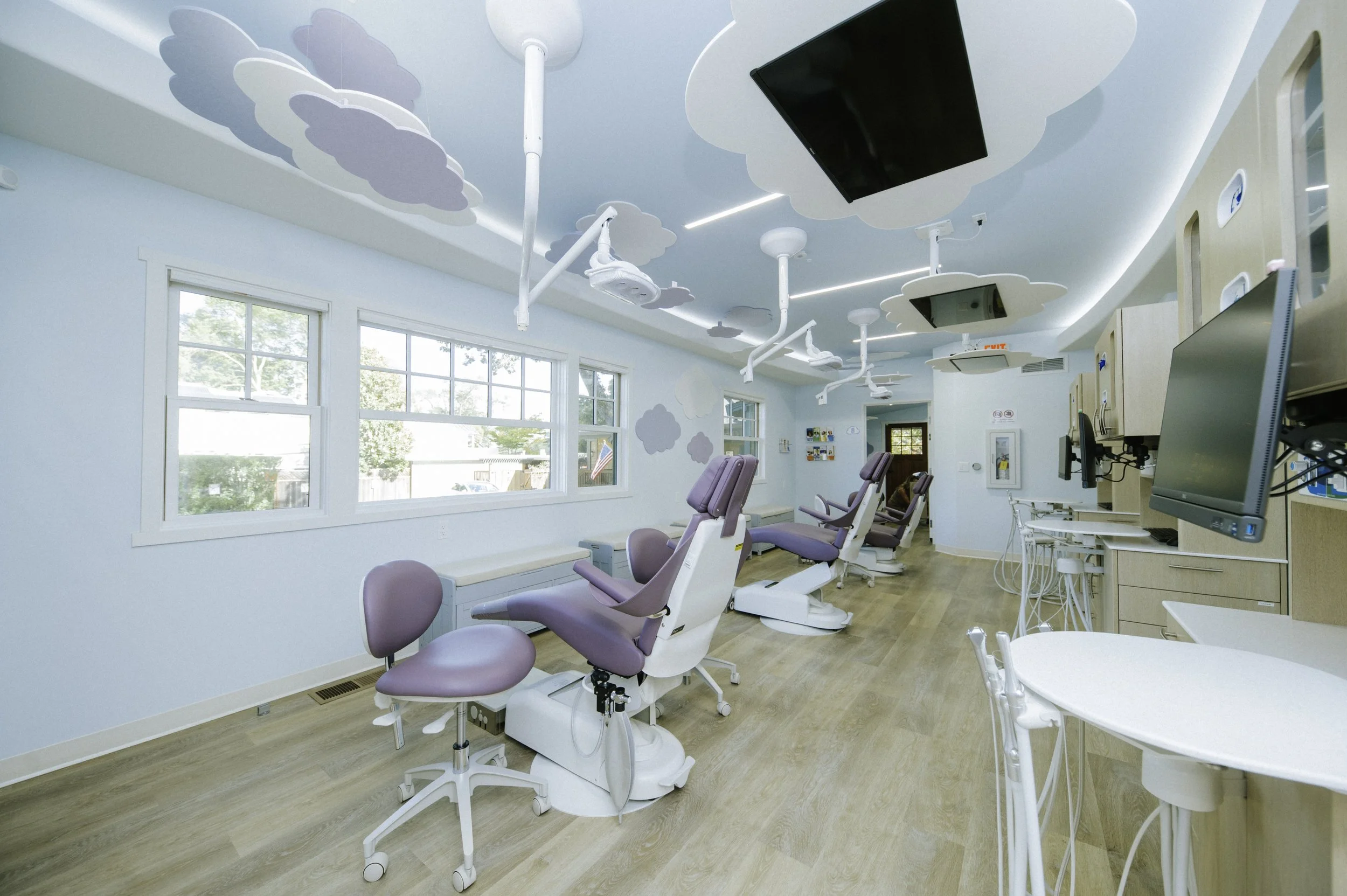 The treatment space for this pediatric practice is an open bay with lavender chairs,
floating clouds and t.v's above the patients.