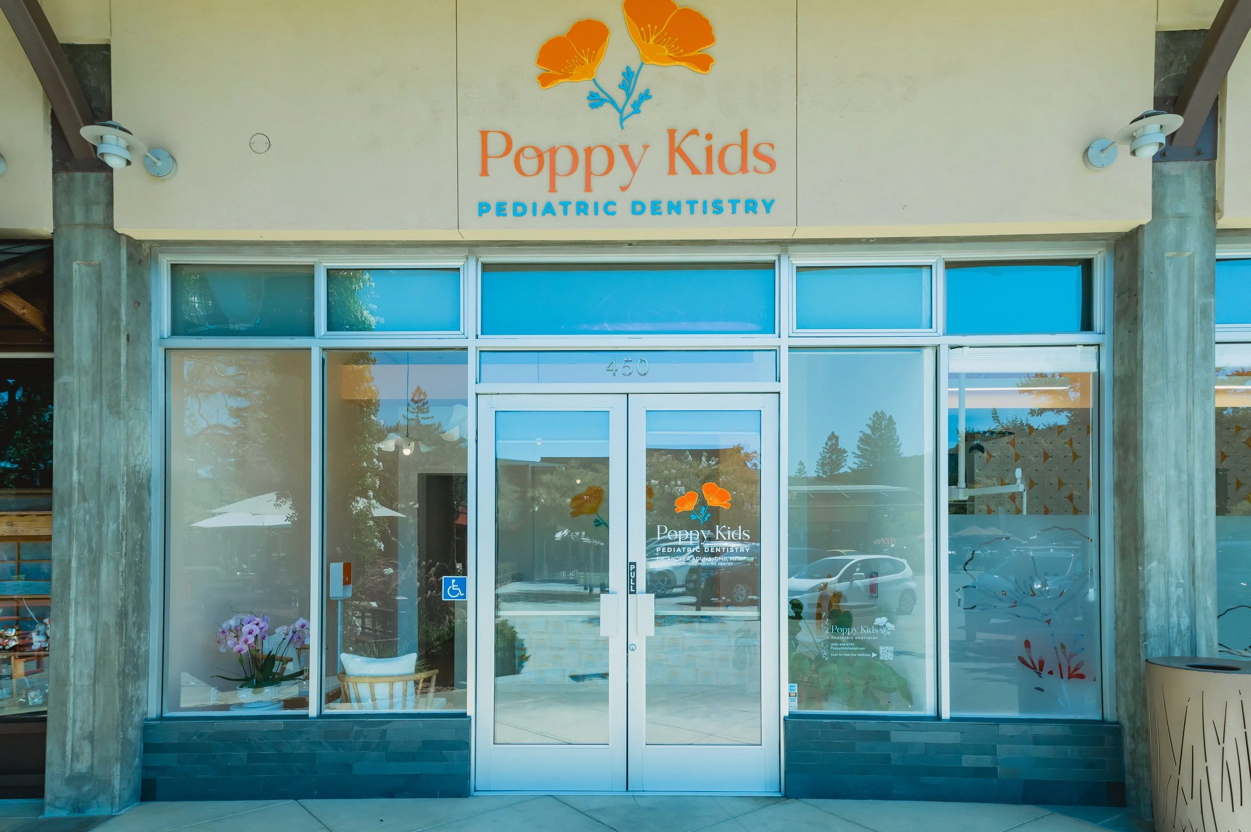 Front view of Poppy Kids Pediatric Dentistry office building with glass entrance doors, floral decor, and signage displaying the clinic's name with orange poppy flowers.