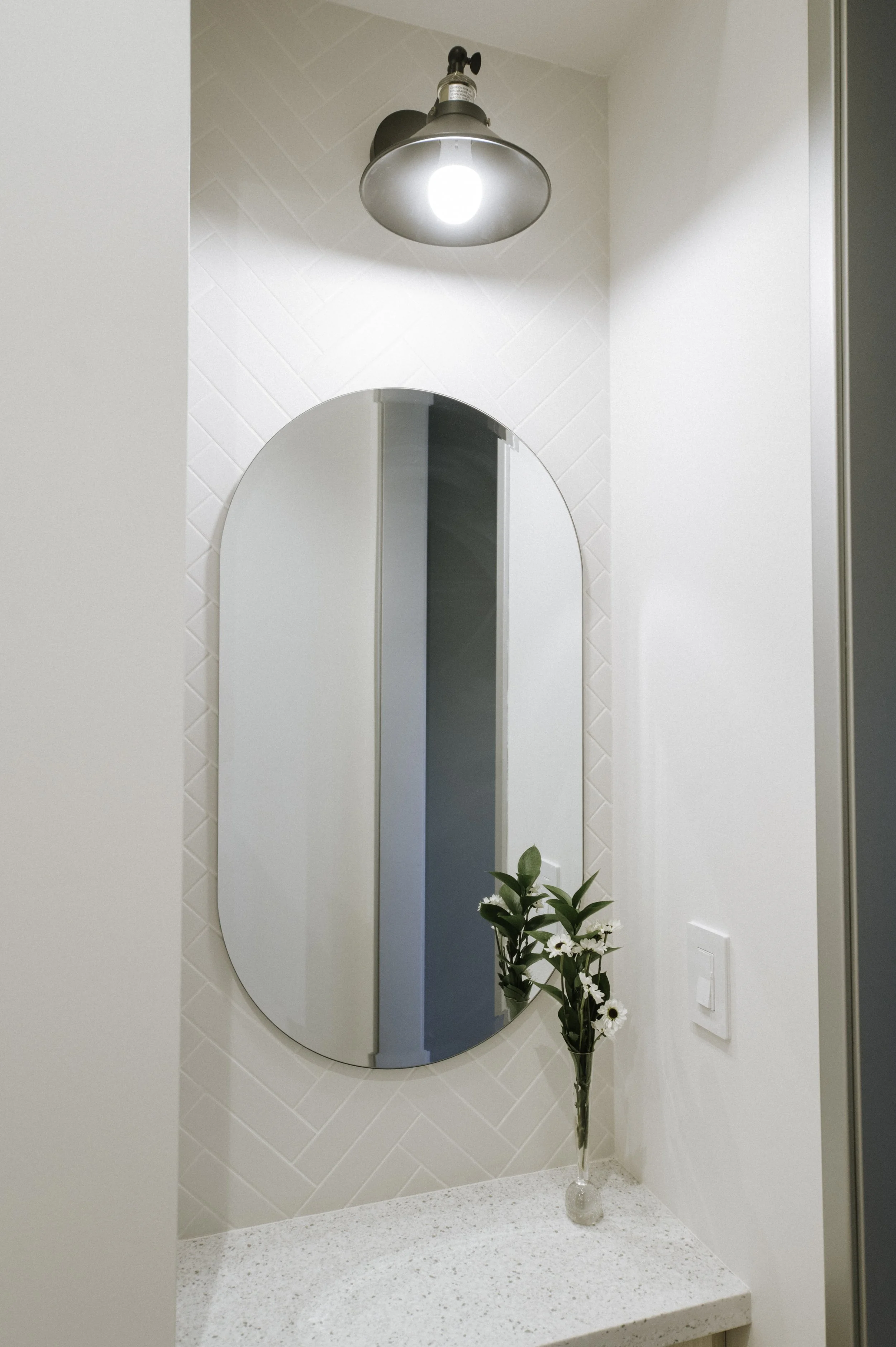 A goodbye mirror is strategically placed on the way to check out. This enables patients to make sure they look o.k before seeing anyone. A farmhouse sconce provides light and style. A cabinet and quartz countertop are topped by a pill shaped mirror.