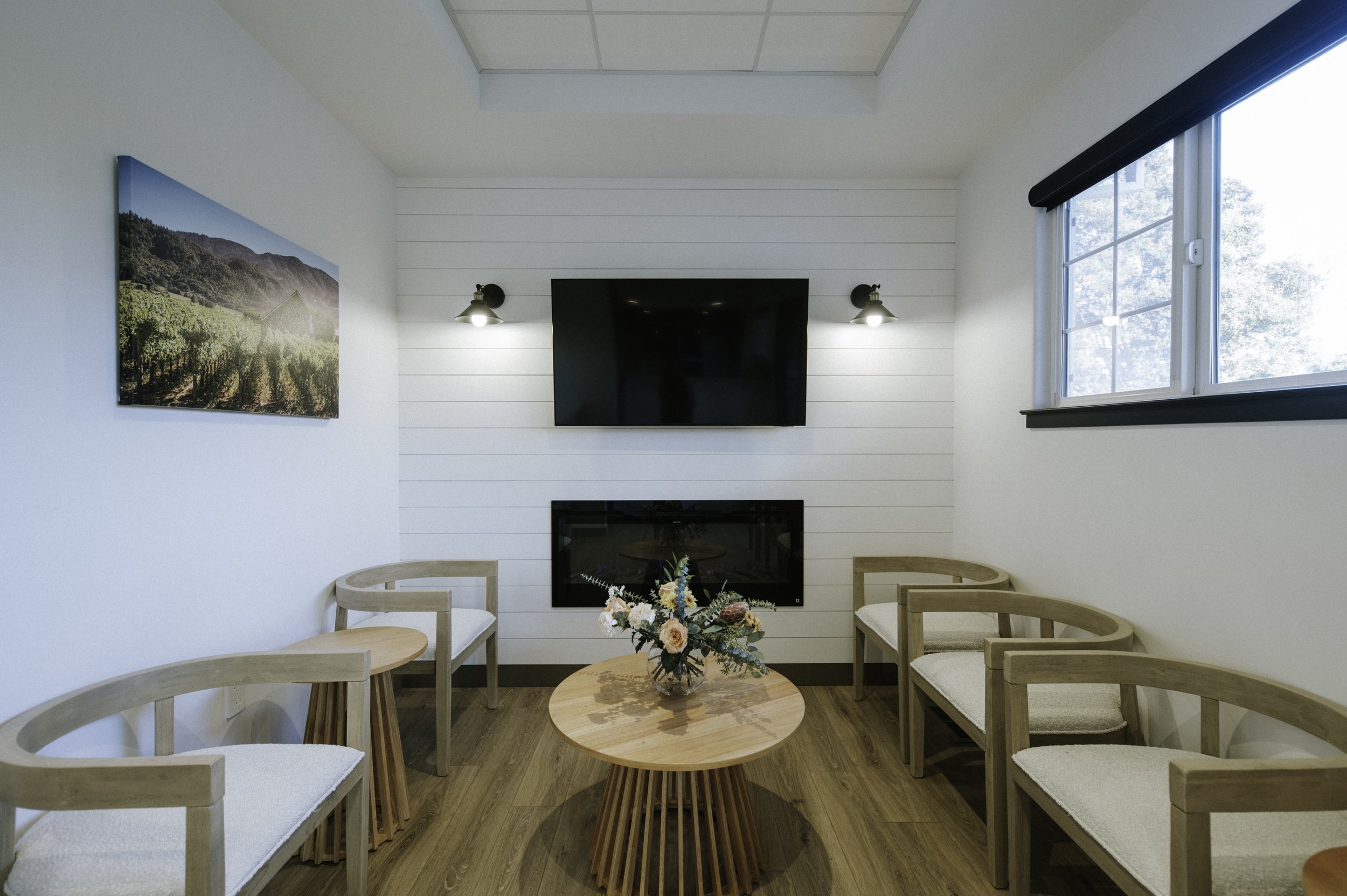 Vineyard inspired artwork, black sconces, warm wood flooring and farmhouse furnishings in the waiting room. A big screen t.v. above the linear fireplace offers extra black hits of color.