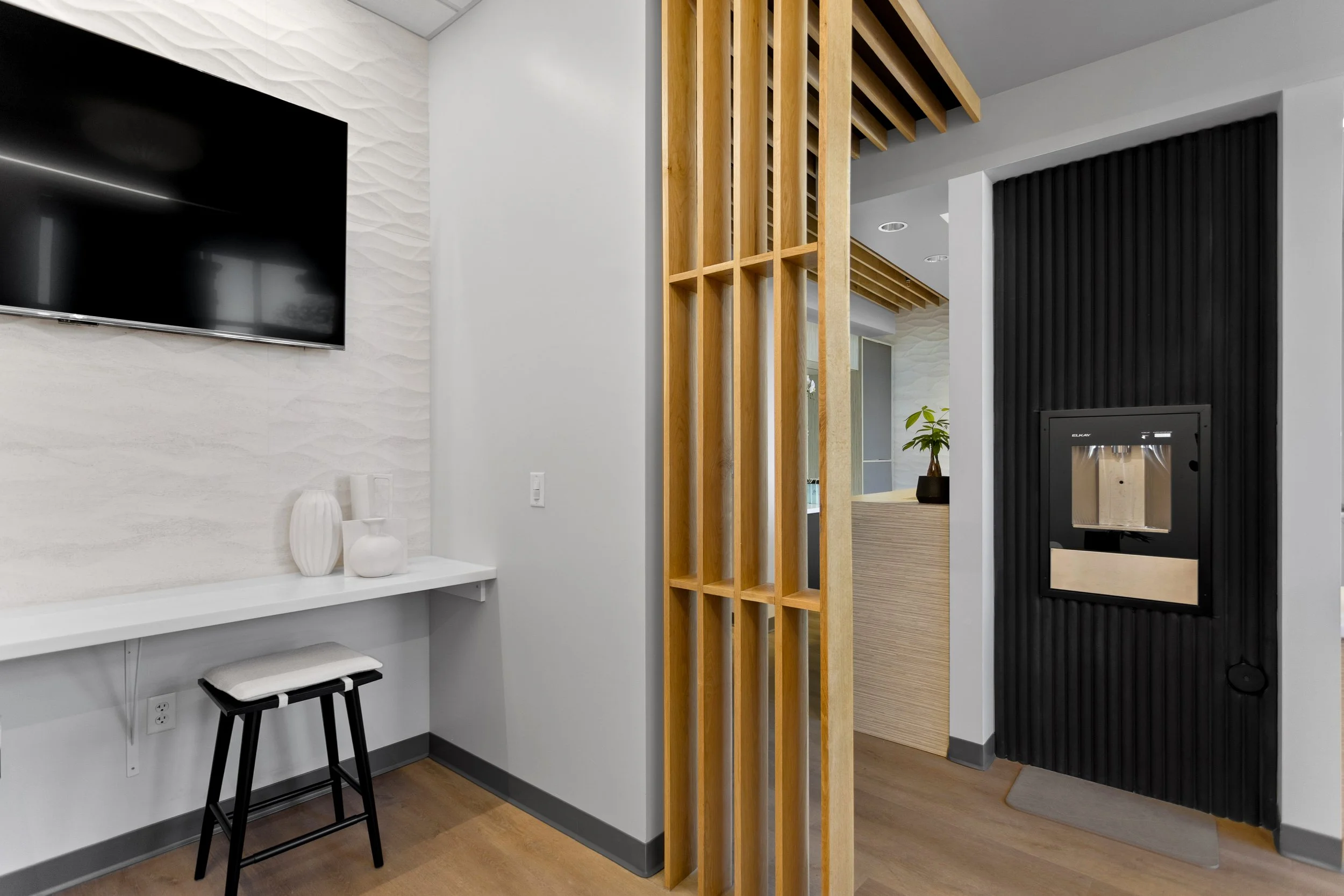 Porcelanosa tile on the walls with a flat screen t.v. over the patient work desk with Japandi style stools. Acoustic wood and bottle filler.