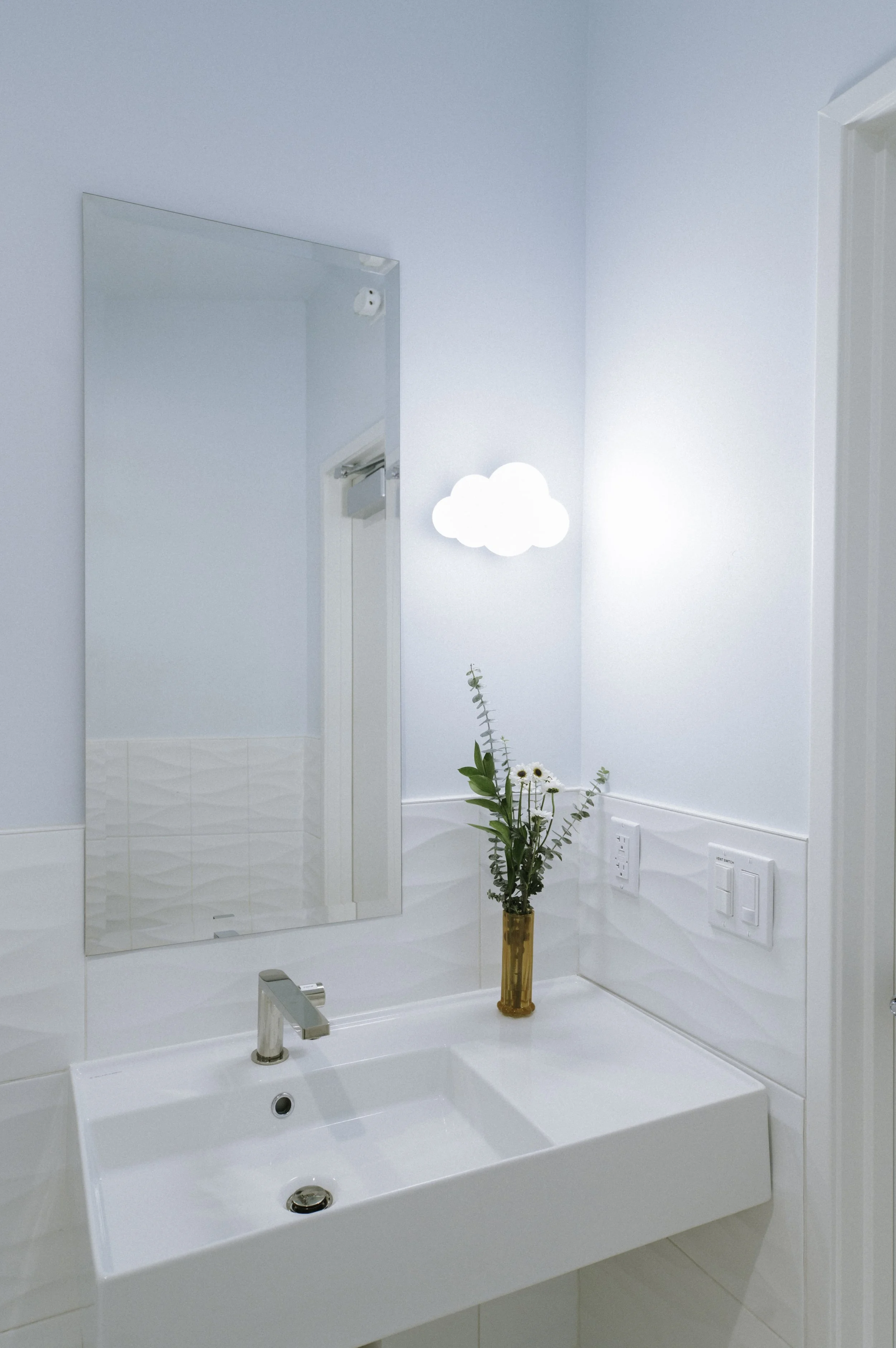 The simple patient restroom features an asymmetric sink and mirror which provides room for a cloud shaped sconce.