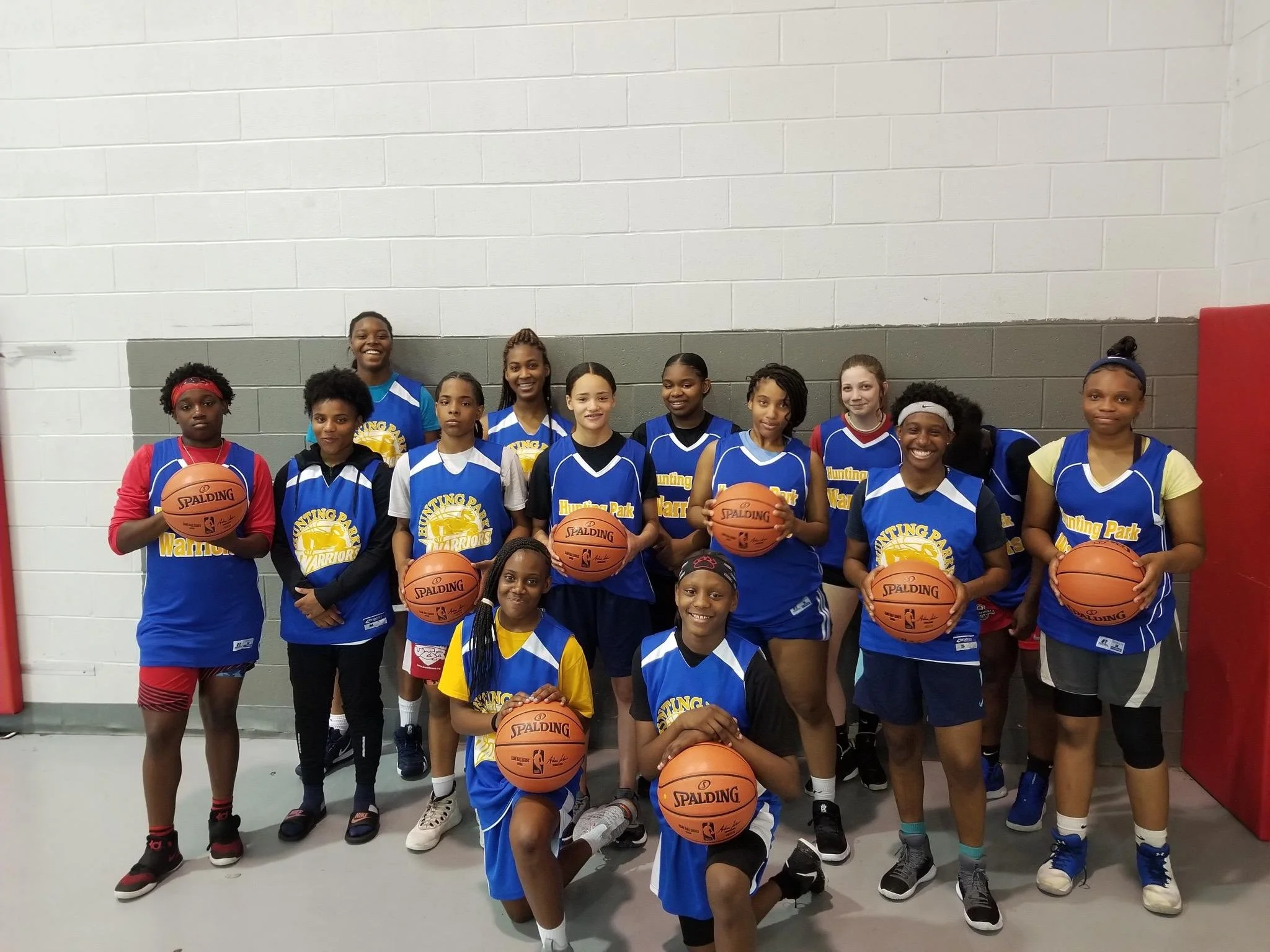 A picture of some of the program youth wearing the blue, yellow and white, uniforms holding a basketball. 