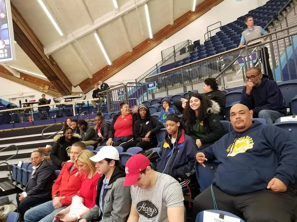 A group of people are in the bleachers, and one of them is wearing a Hoodie with Hunting Park Warriors. 