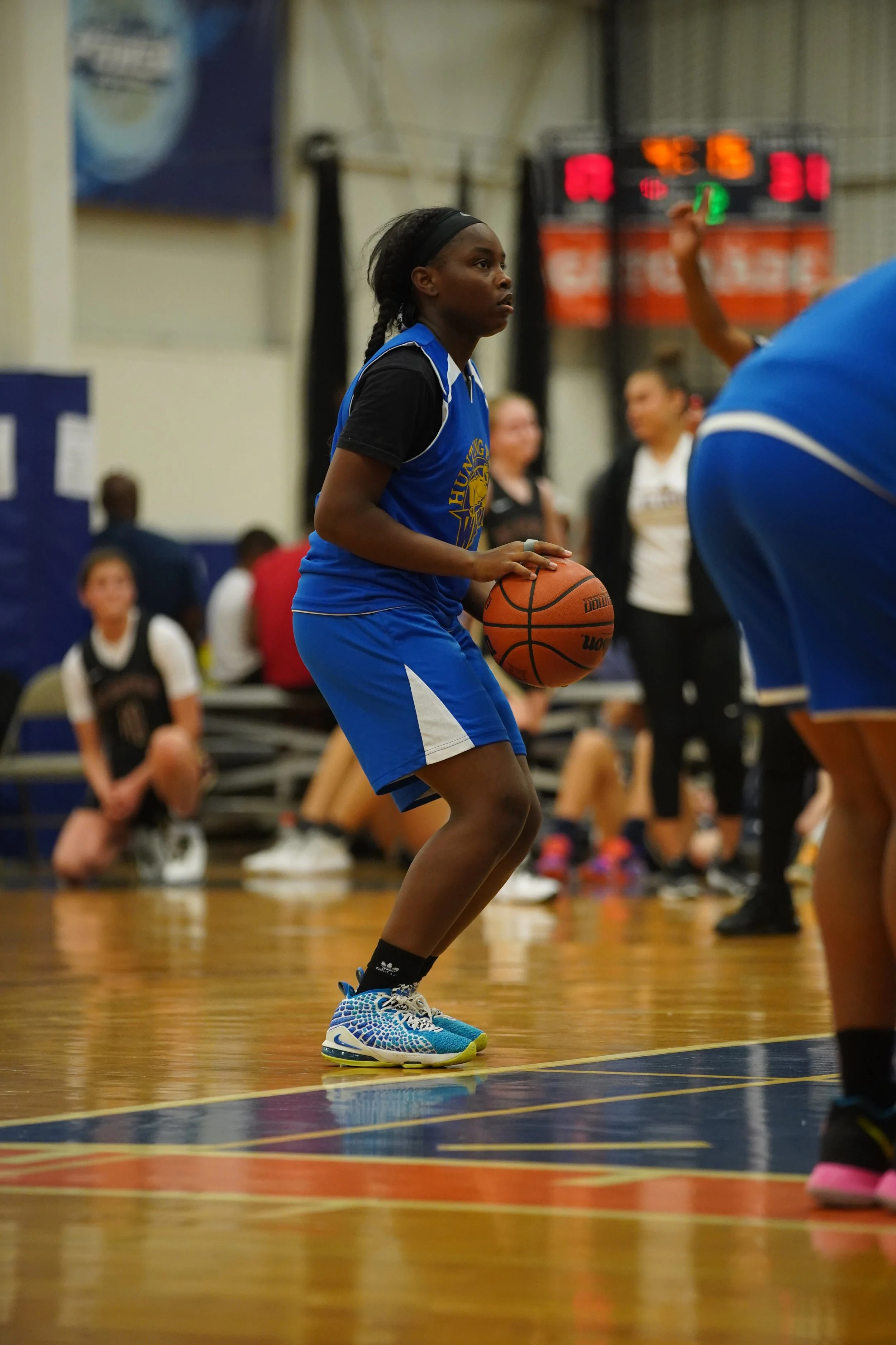A black young girl, wearing black, white and blue basketball gear. Ready to shoot the basketball. 