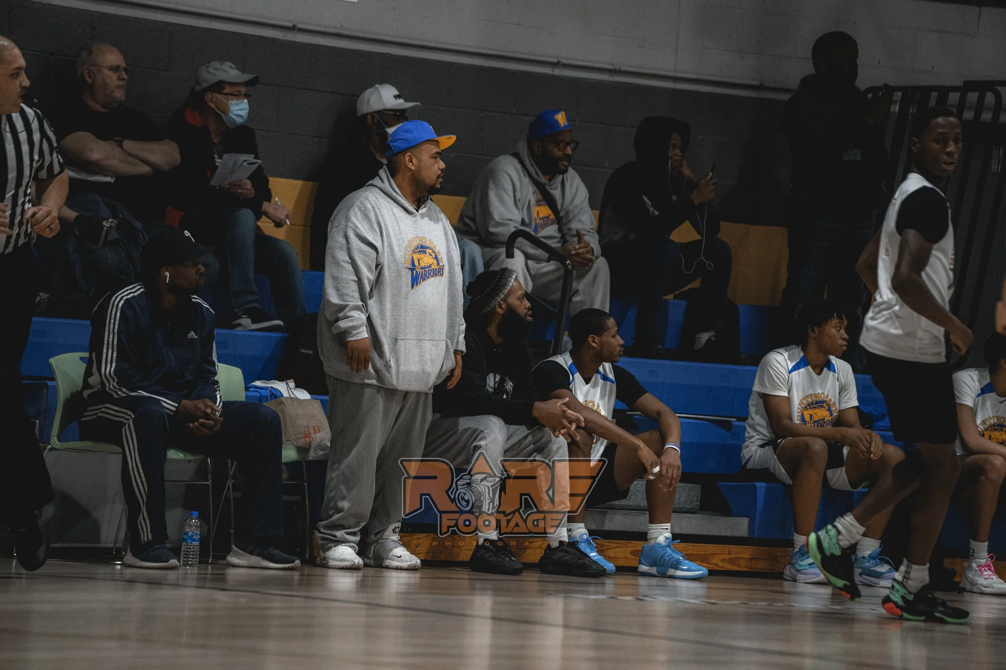 A Male basketball coach, wearing grey, white and yellow hoodie. 