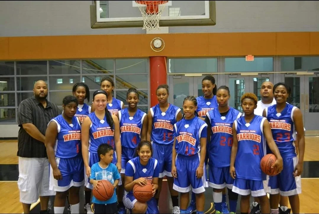 An all-female youth basketball team, wearing blue and white uniforms. The coaches stand on the left and right of the pictures. 