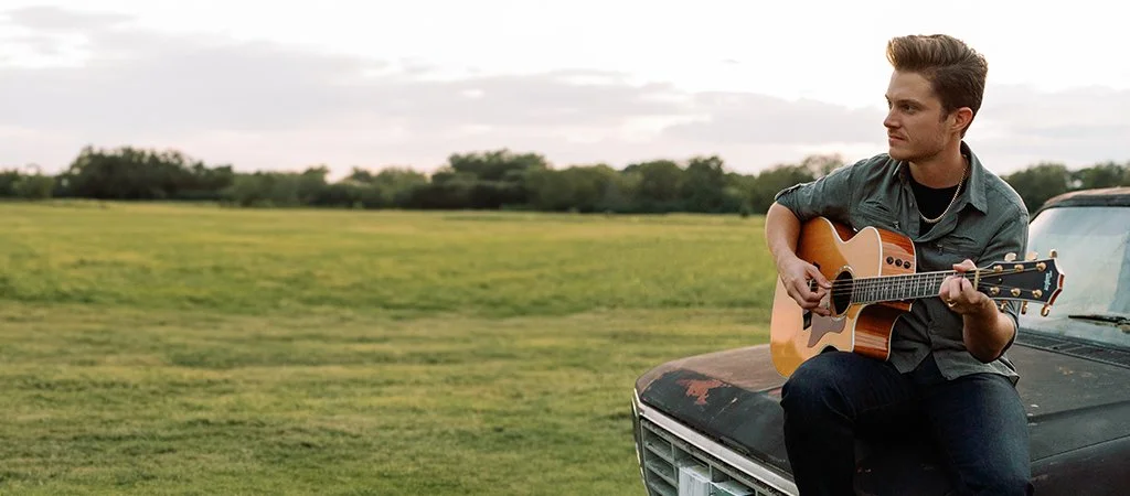 Creigh Riepe playing acoustic guitar beside a vintage truck