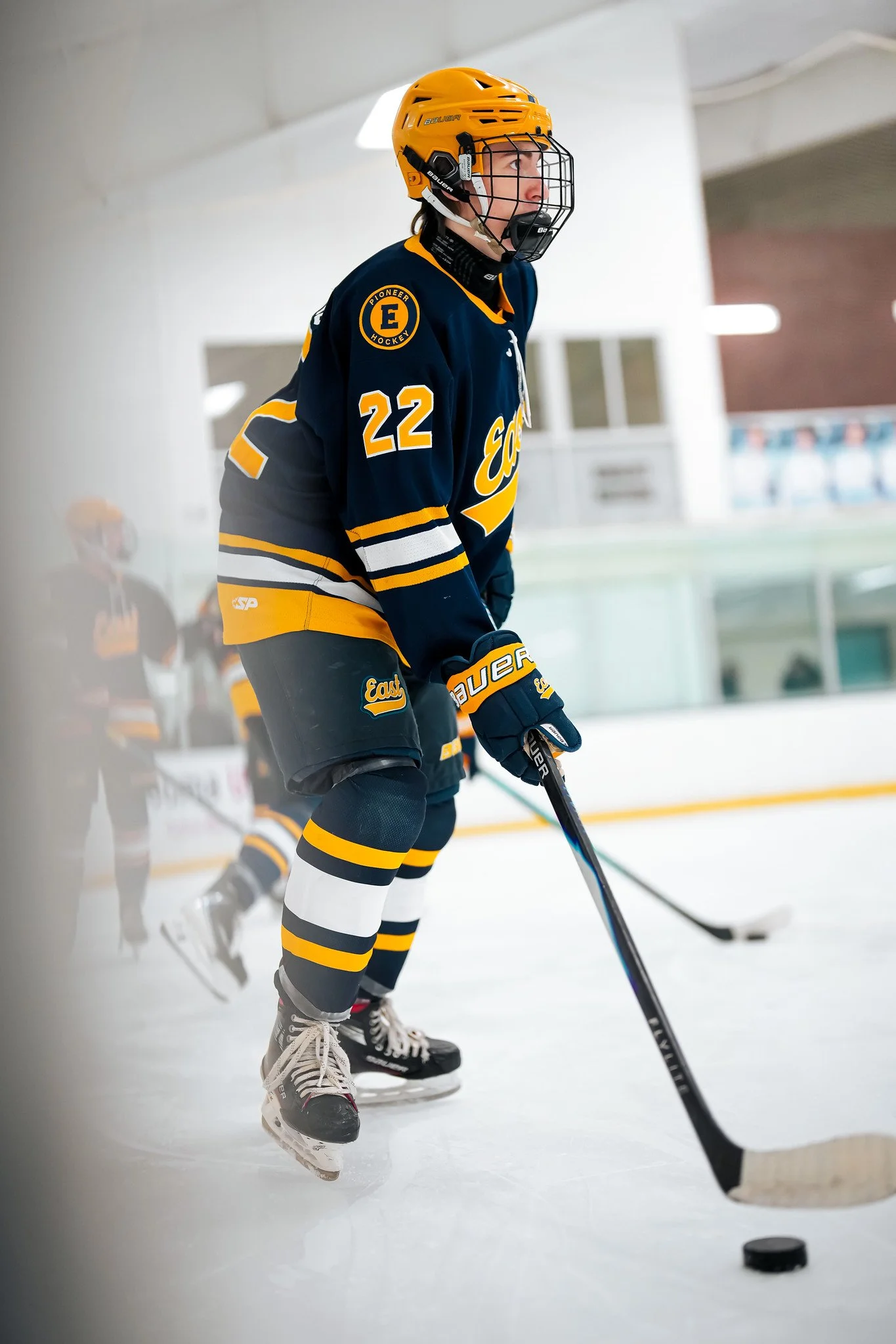 An ice hockey player wearing a yellow helmet and a navy blue and yellow jersey with the number 22, on an ice rink, preparing for a game or practice.