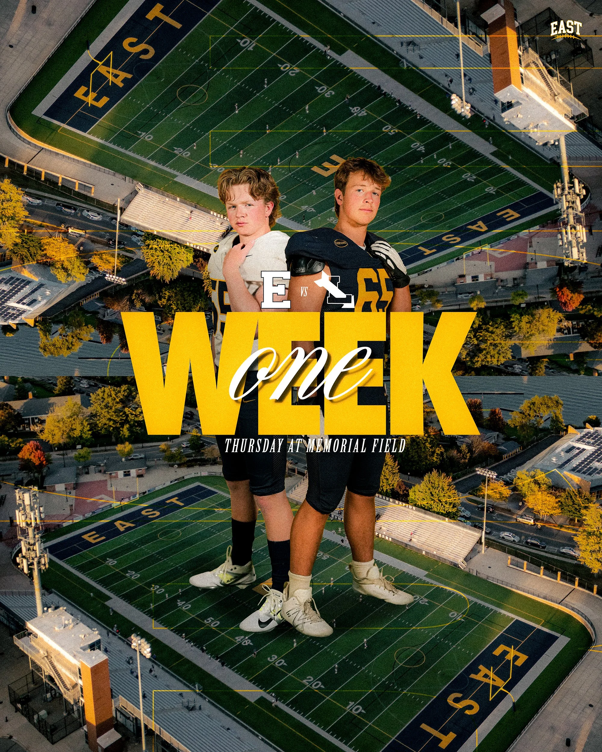 An aerial view of a football field with two young male football players. One player is in a white uniform and the other in a black uniform. The football field is marked with yard lines and the word 'EAST' at the end zones. The players are positioned 
