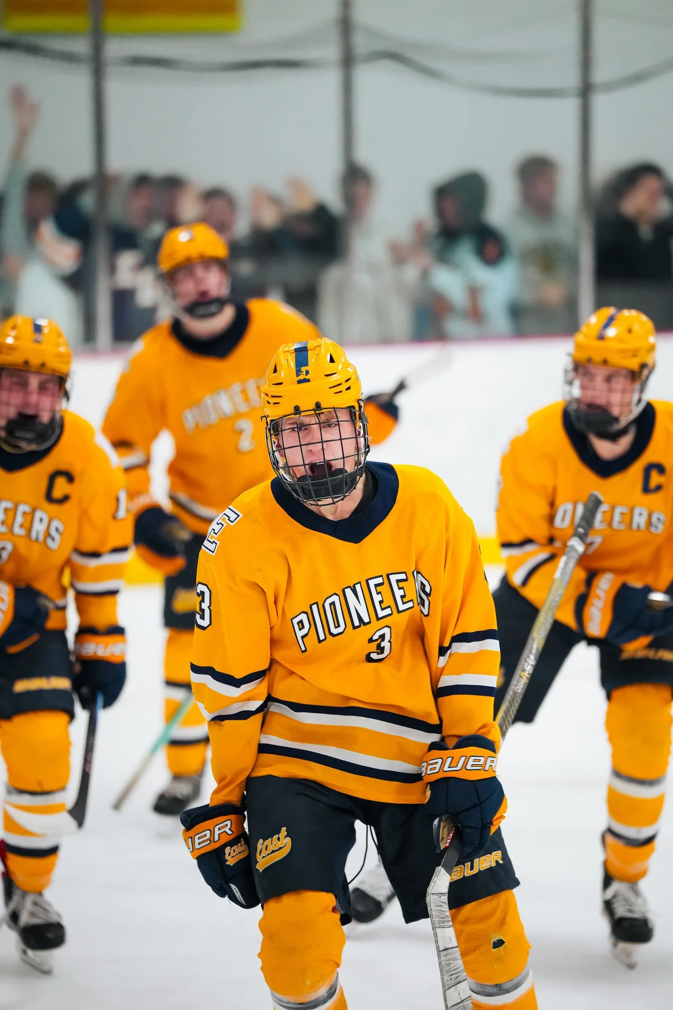 Youth hockey team in yellow jerseys celebrating on the ice rink, with some players raising their arms in the background.