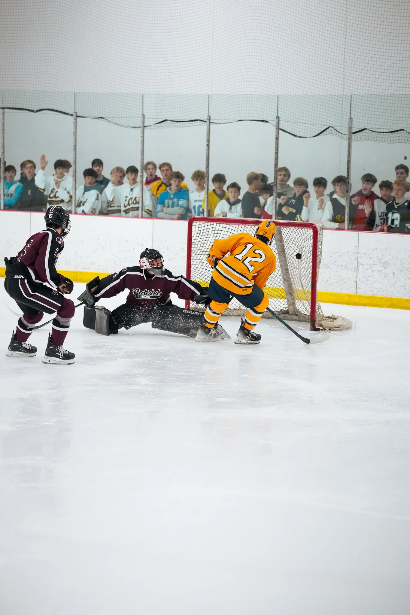 A hockey game with players near the net and spectators watching from behind the glass.