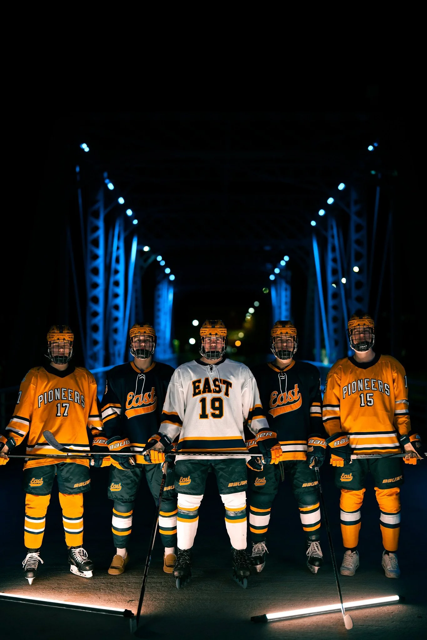 Ice hockey team standing together in uniform on a dark, illuminated bridge at night.