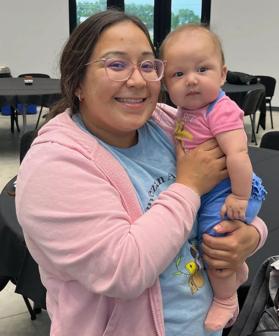 a smiling woman with glasses in a pink jacket holding a baby in a pink and blue outfit, positioned beneath the blue title "Indigenous Family, Friend, Neighbor Child Care Network (FFN)."