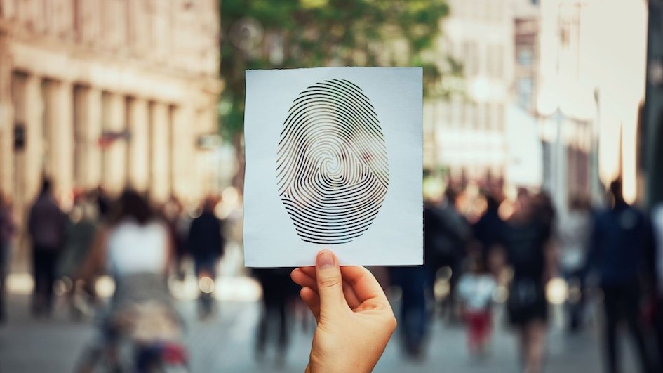 Hand holding a white piece of paper with a large finger print on it in front of a faded background of a busy street