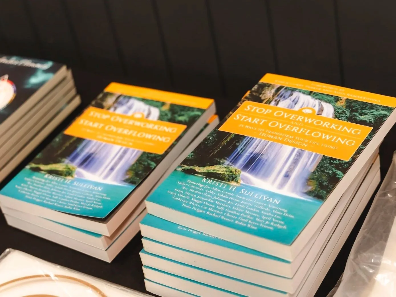 Stacks of books titled 'Stop Overworking and Start Overflowing' on a table.