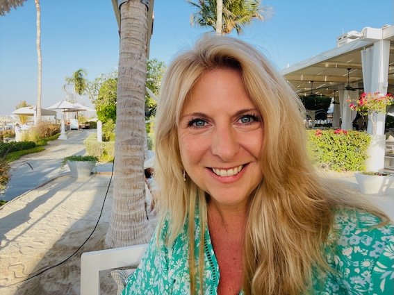Amber Clements looking at camera wearing green top with beach and palm trees in the background.