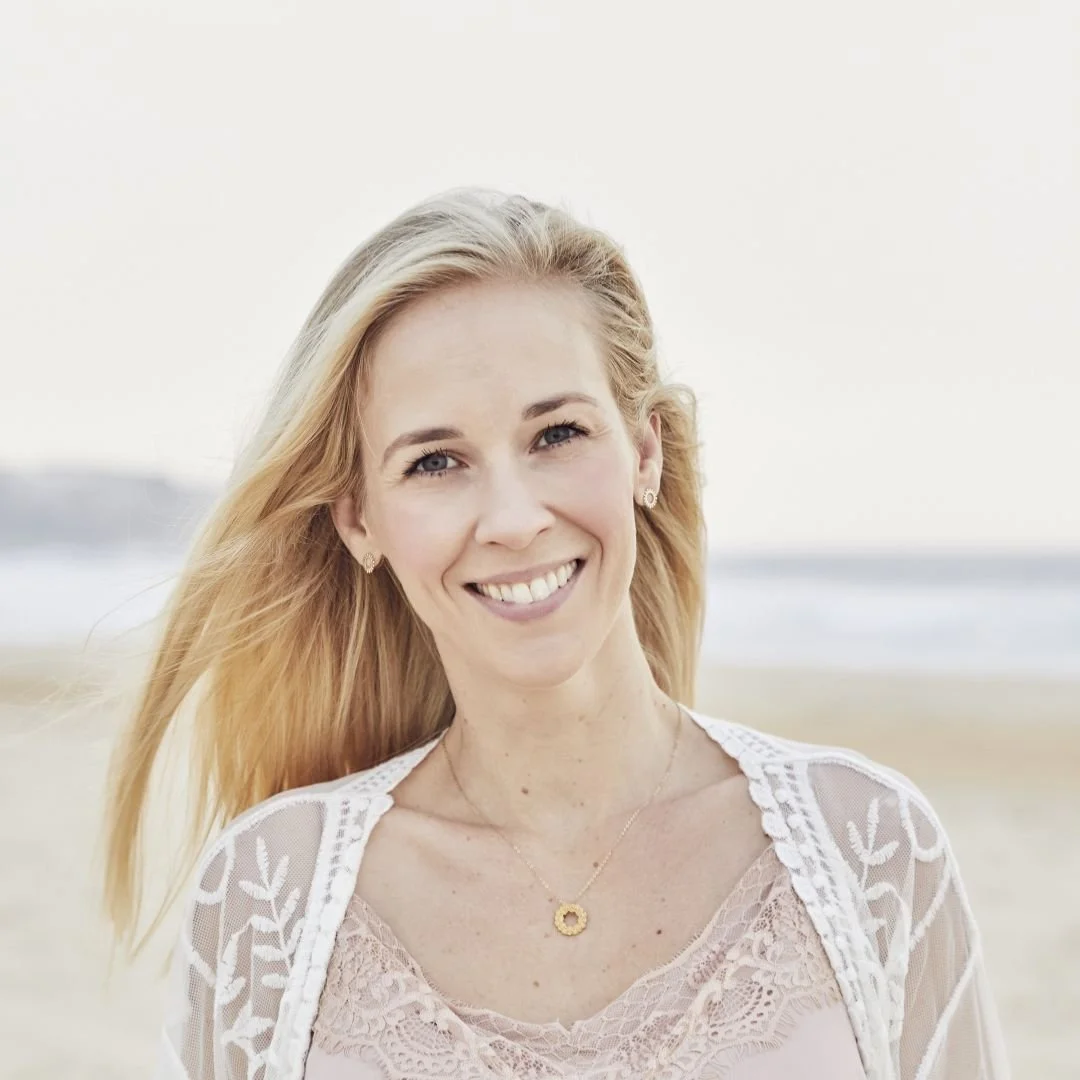 A woman with long blonde hair smiling on a beach.