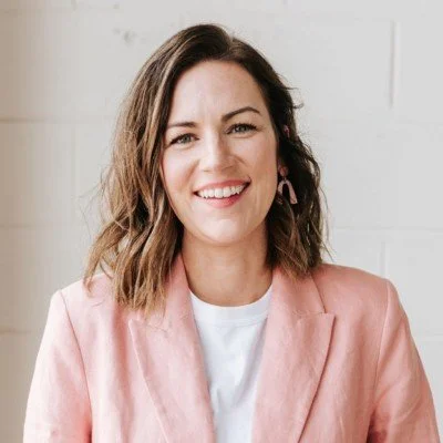 Courtney wearing a pink blazer and white t-shirt in front of pale background