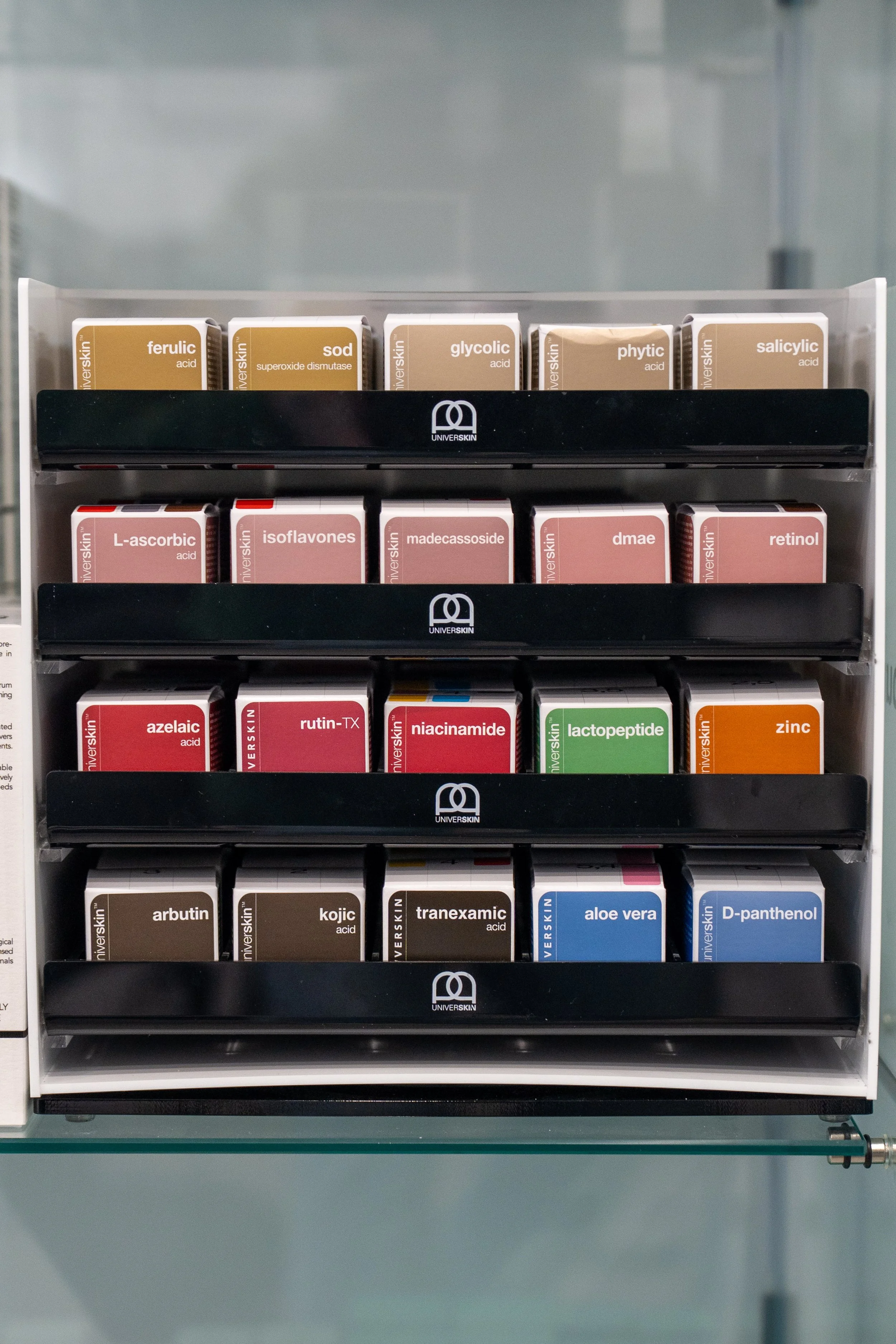 Shelf with various pharmaceutical boxes, including acids, niacinamide, aloe vera, D-panthenol, and zinc, organized in rows.