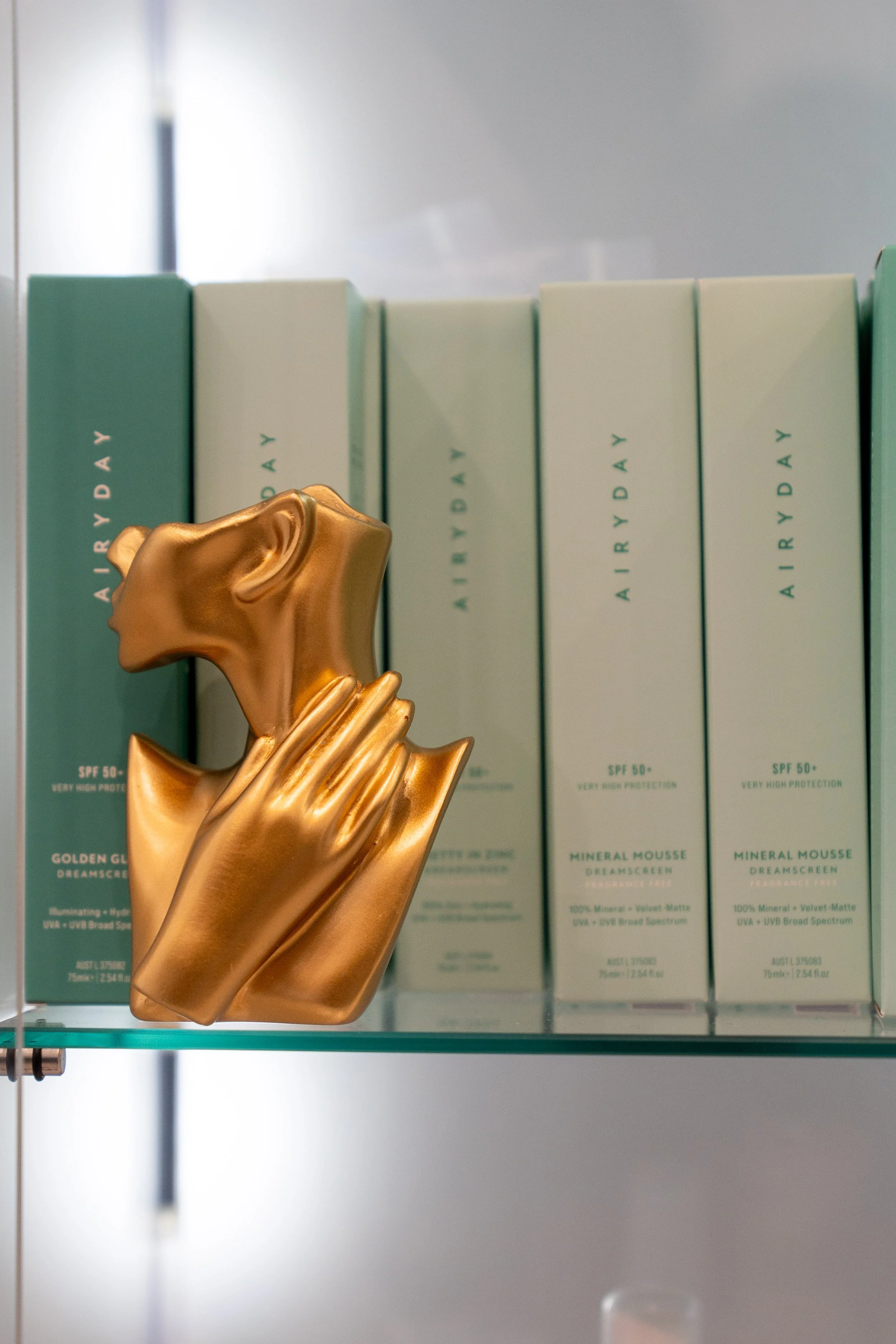 Display of skincare products in light green packaging labeled 'Airy Day,' with gold-colored hand-shaped mannequin in the foreground.