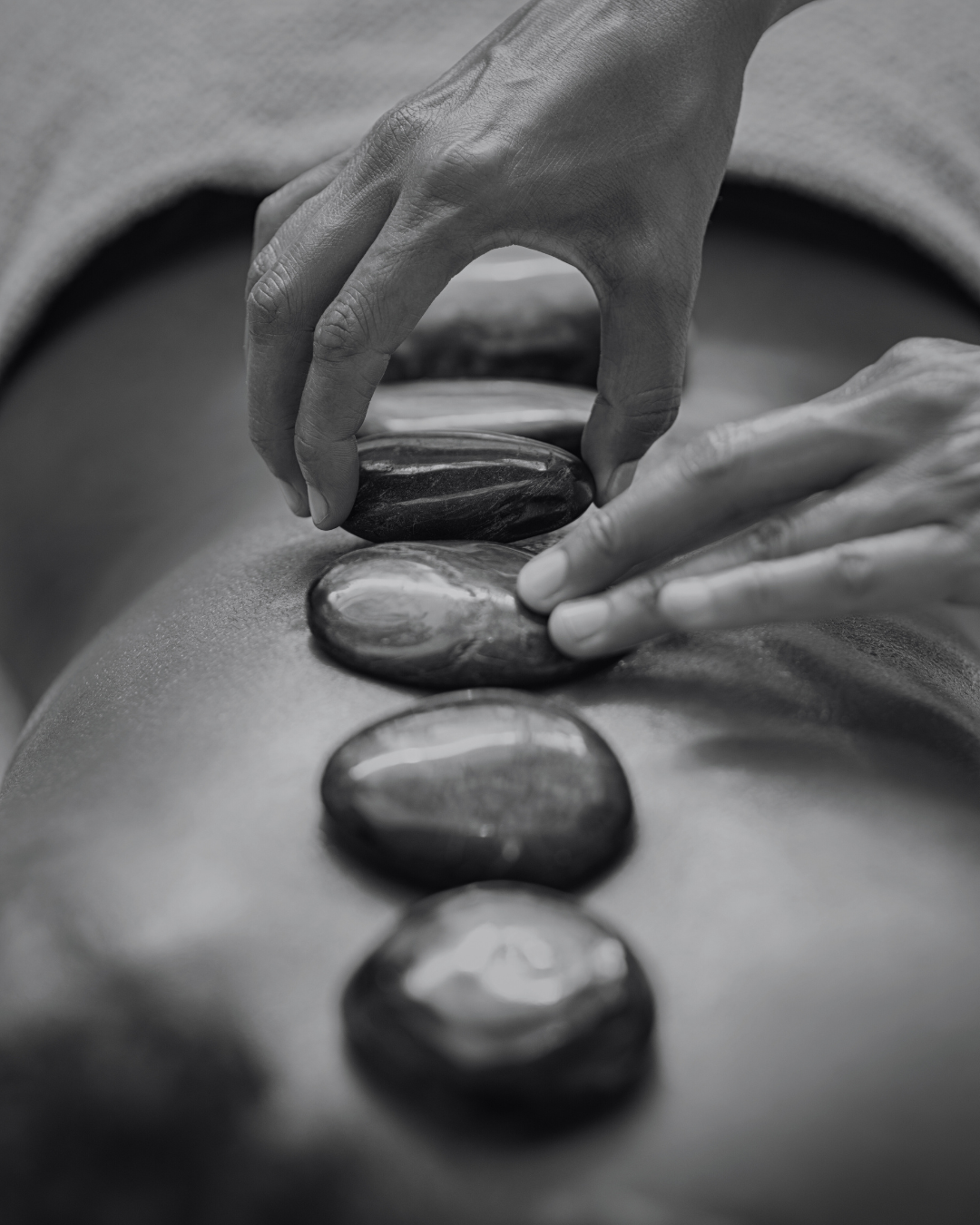 A person is placing smooth stones along the back of another person during a hot stone massage therapy session.