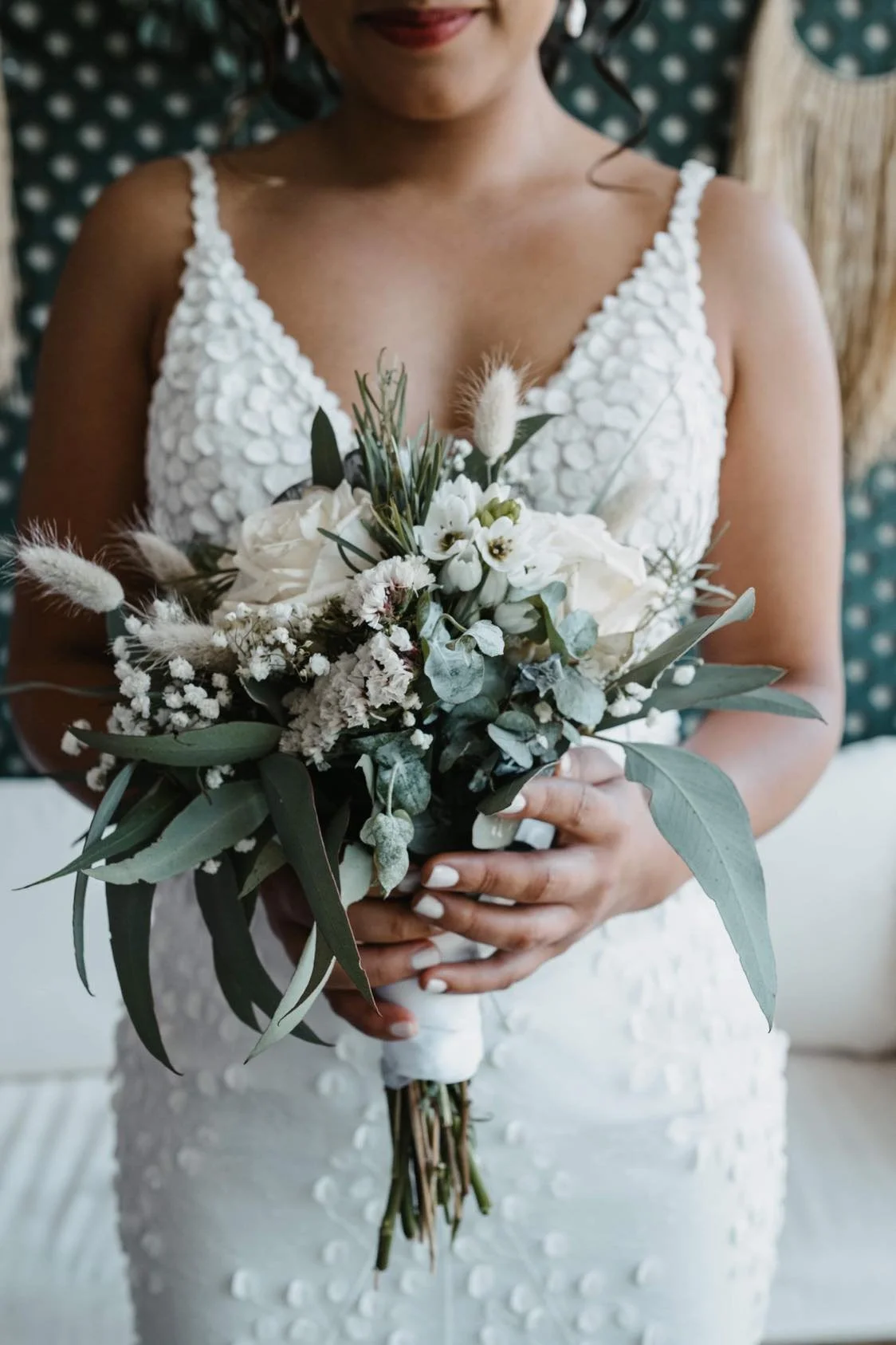 A woman in a white dress holding a bouquet of white and green flowers.