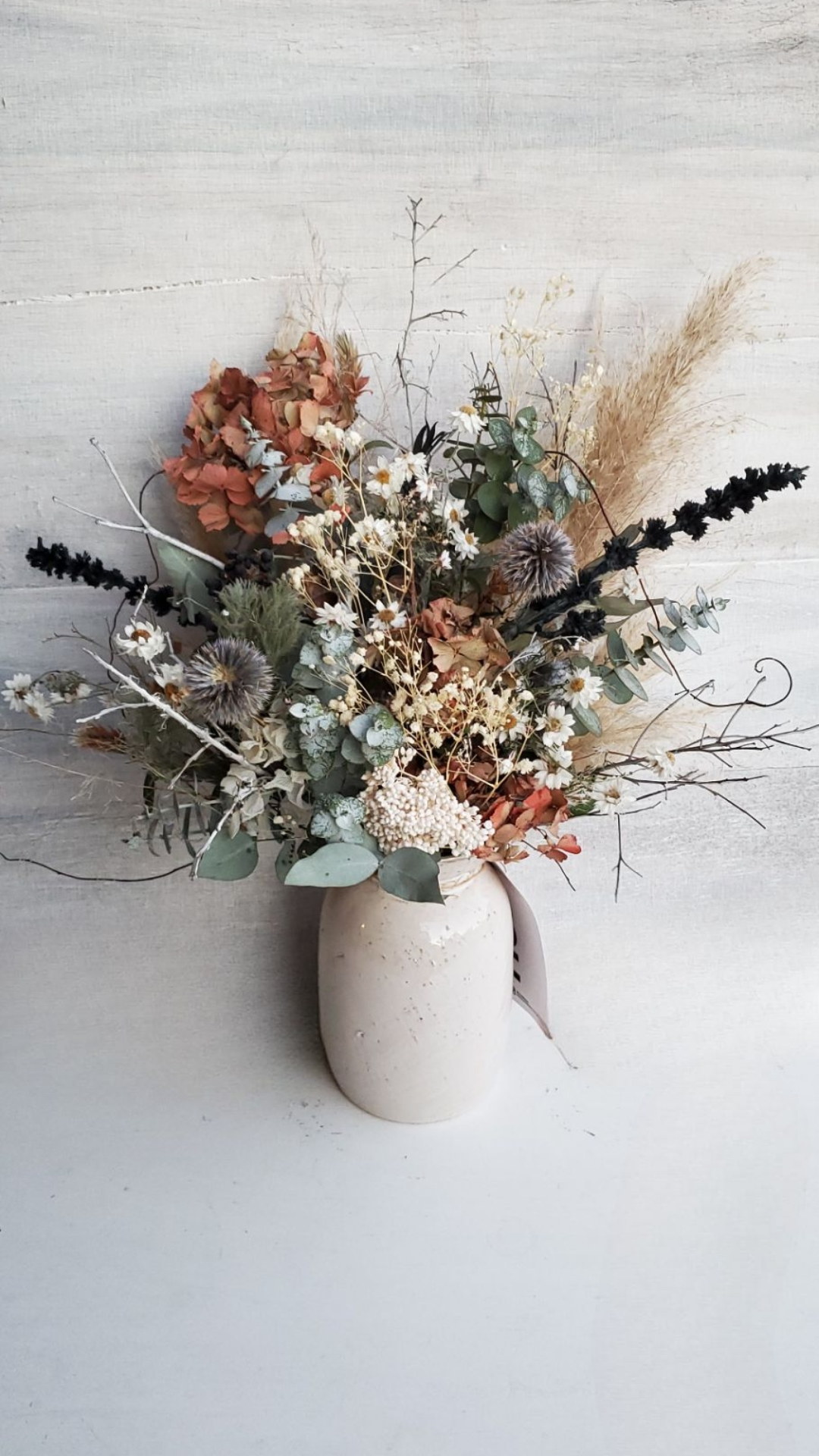 A bouquet of dried flowers in a white vase against a light wooden background.