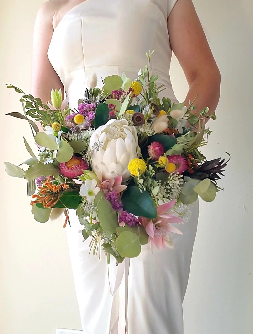 A woman in a white dress holding a large colorful bouquet of flowers.