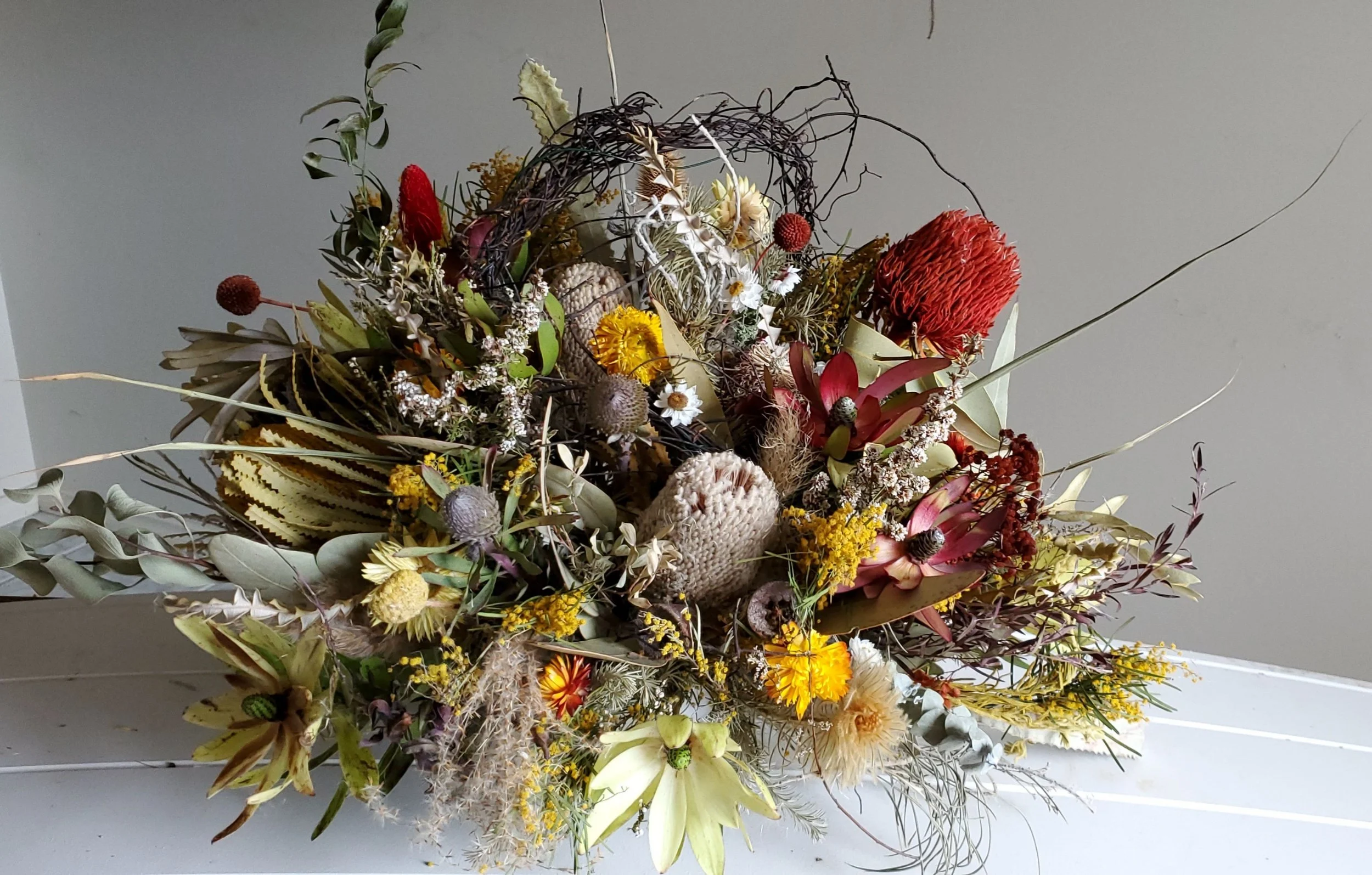 An arrangement of dried flowers including various colored blooms, seed pods, and foliage in a natural, rustic style.