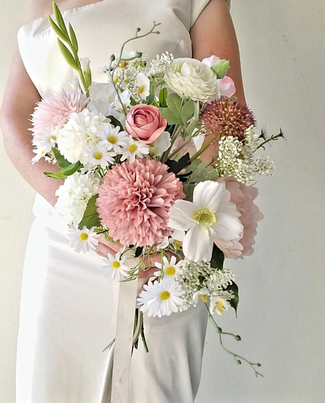 Person in white dress holding a bouquet of pink, white, and green flowers.