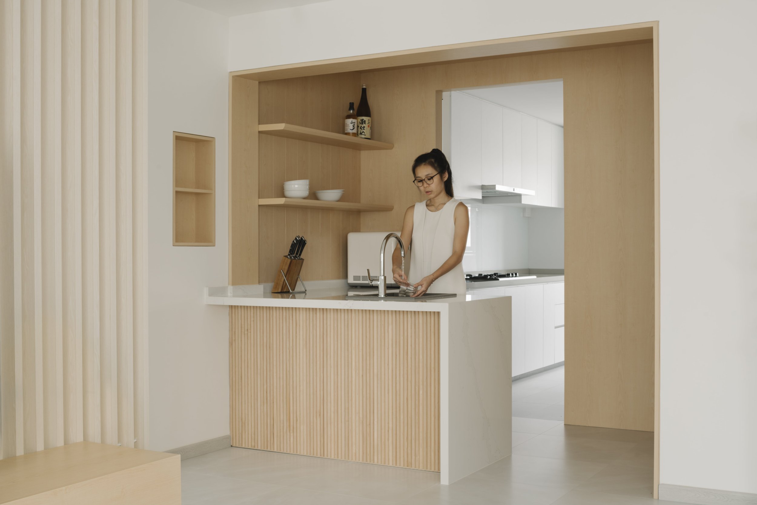 Bright minimalist kitchen with natural wood accents and a fluted island counter, showcasing modern Singapore home design.