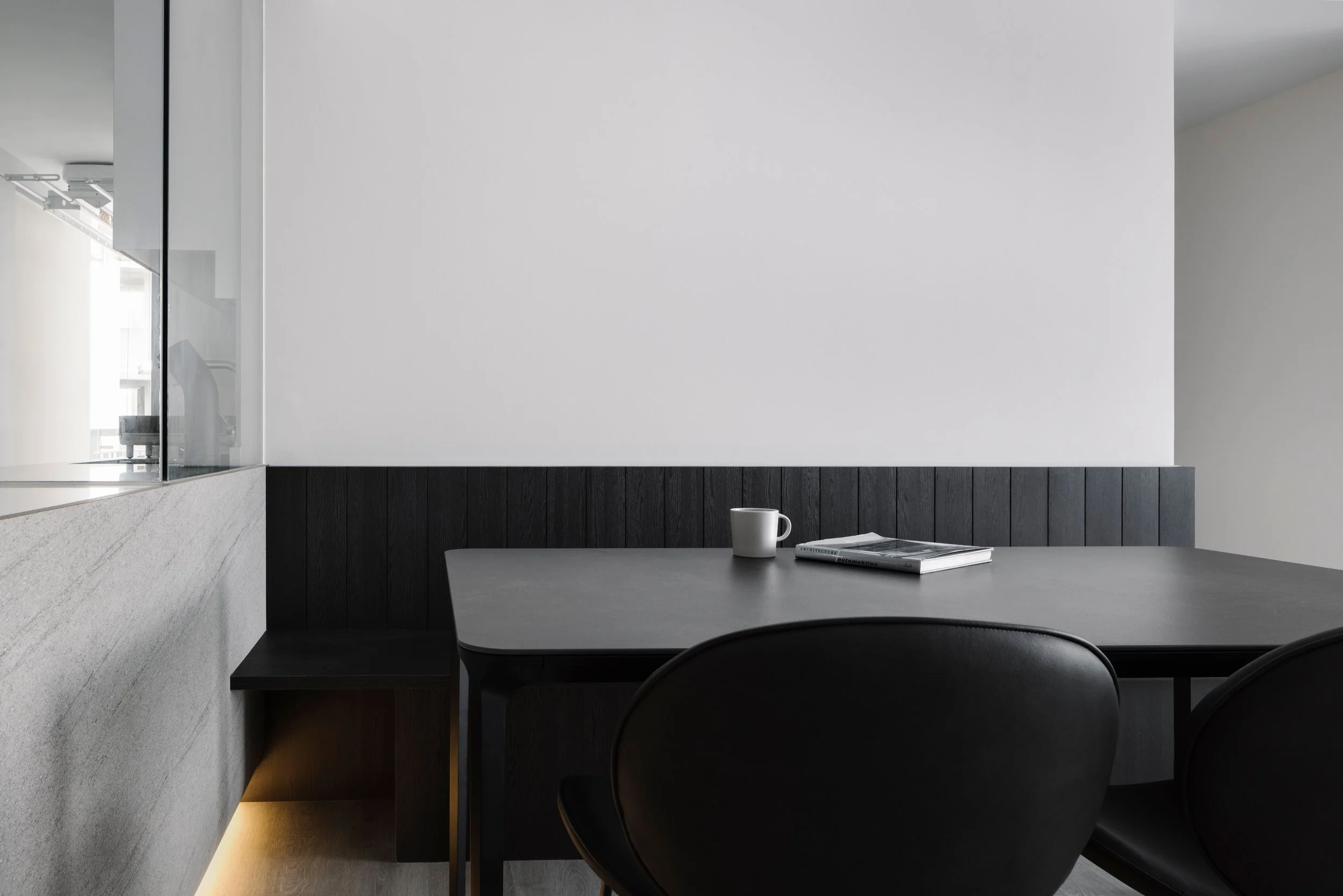 Modern dining corner with black table, vertical upholstered bench and warm under-bench lighting against a clean white wall.
