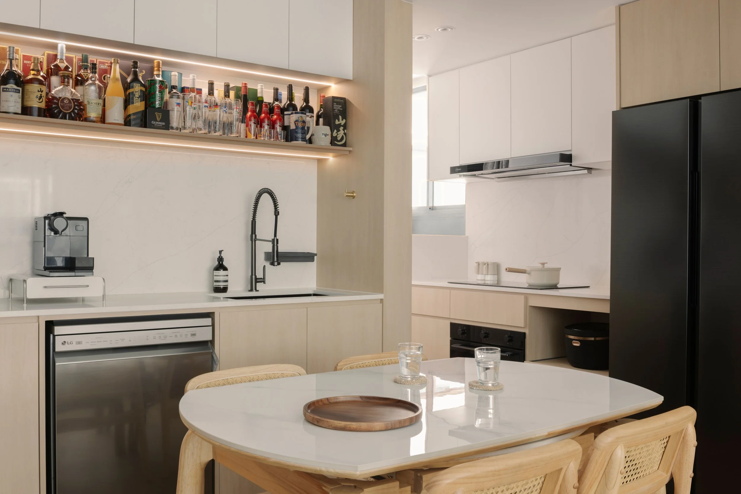 Modern open-concept kitchen with integrated home bar, marble backsplash, black appliances, and minimalist dining area in a contemporary home interior.