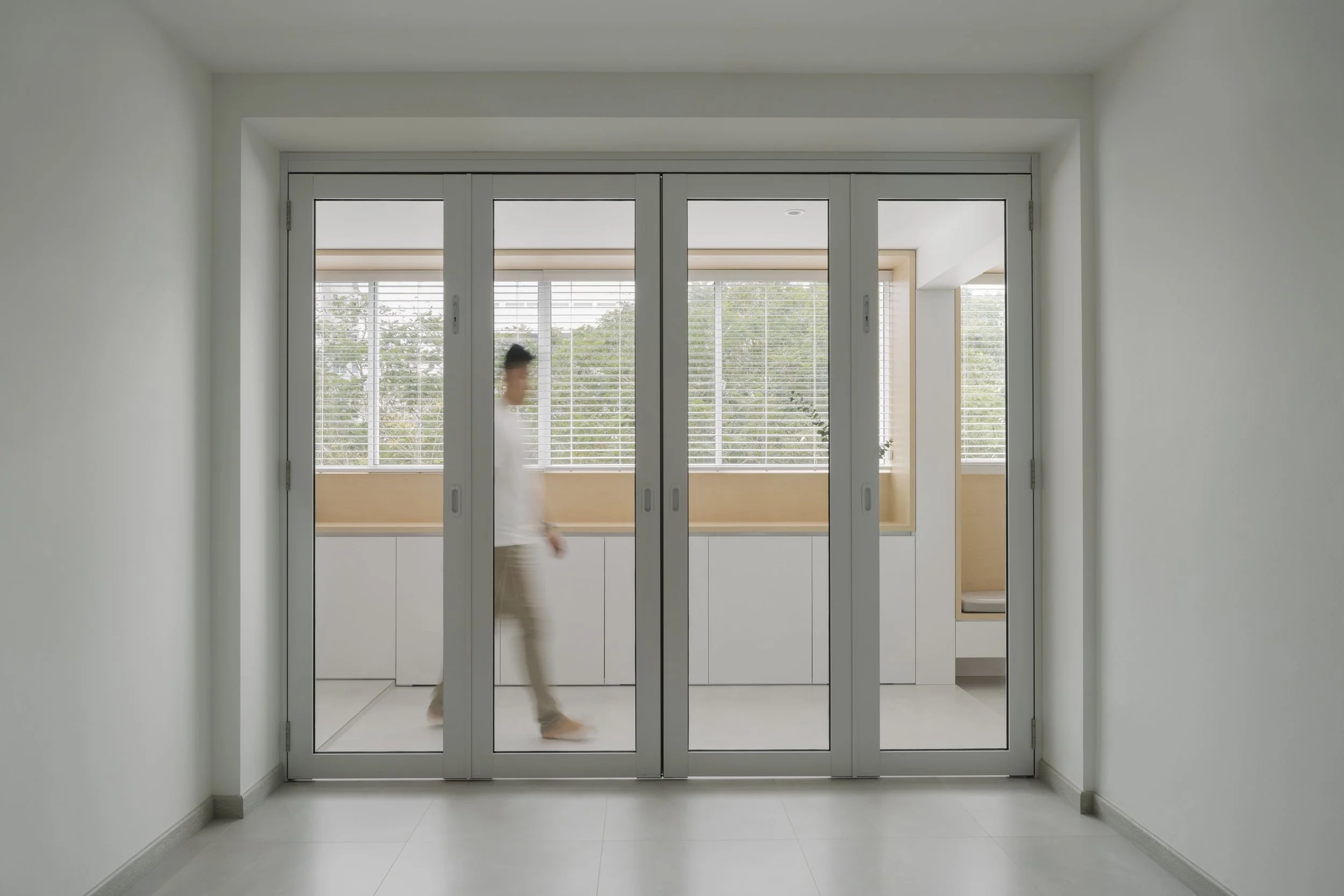 Minimalist glass door partition with aluminium frames, showing a walking silhouette behind the closed sliding doors.