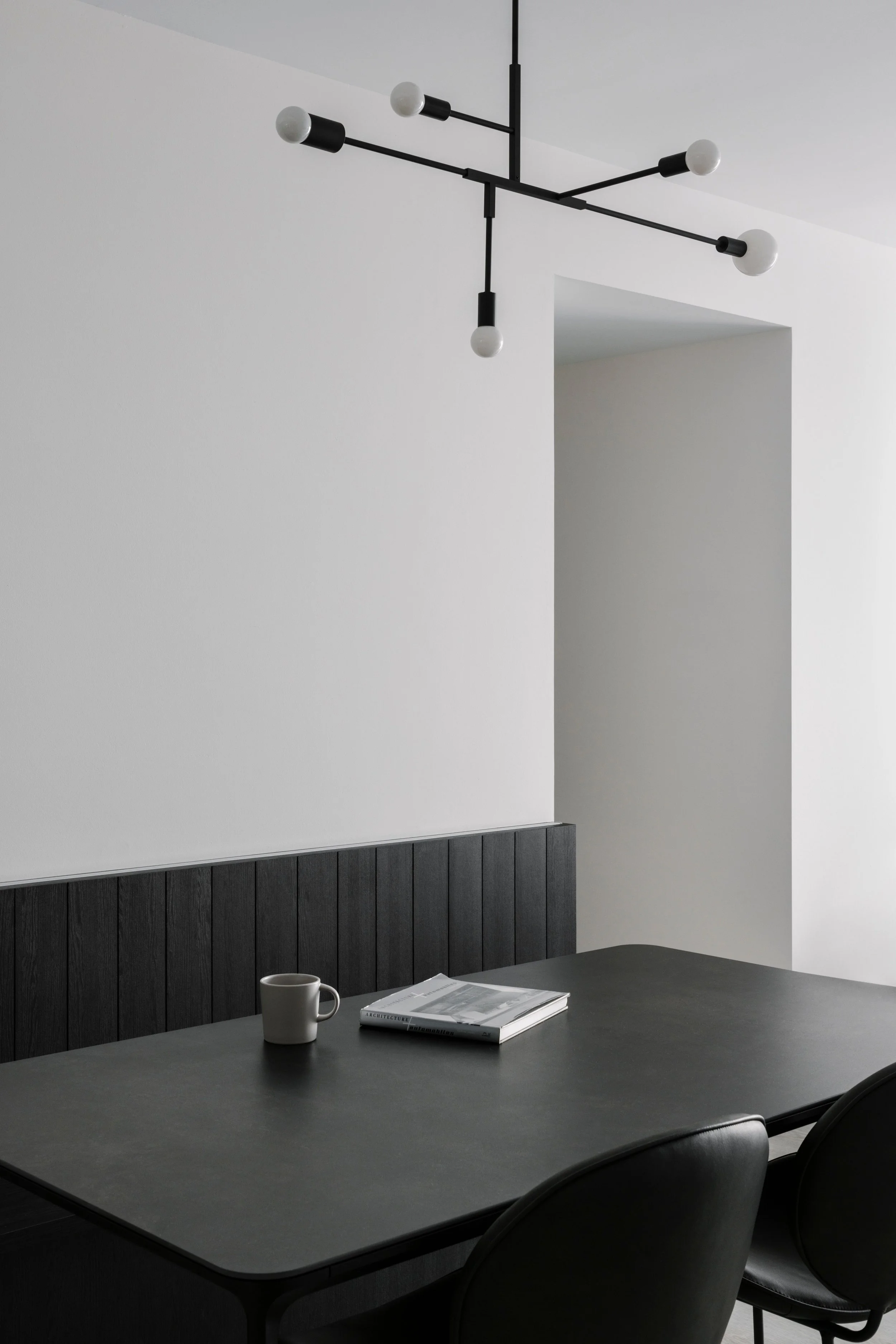 Modern dining area with a black table, vertical upholstered bench and contemporary linear ceiling light in a clean white interior.