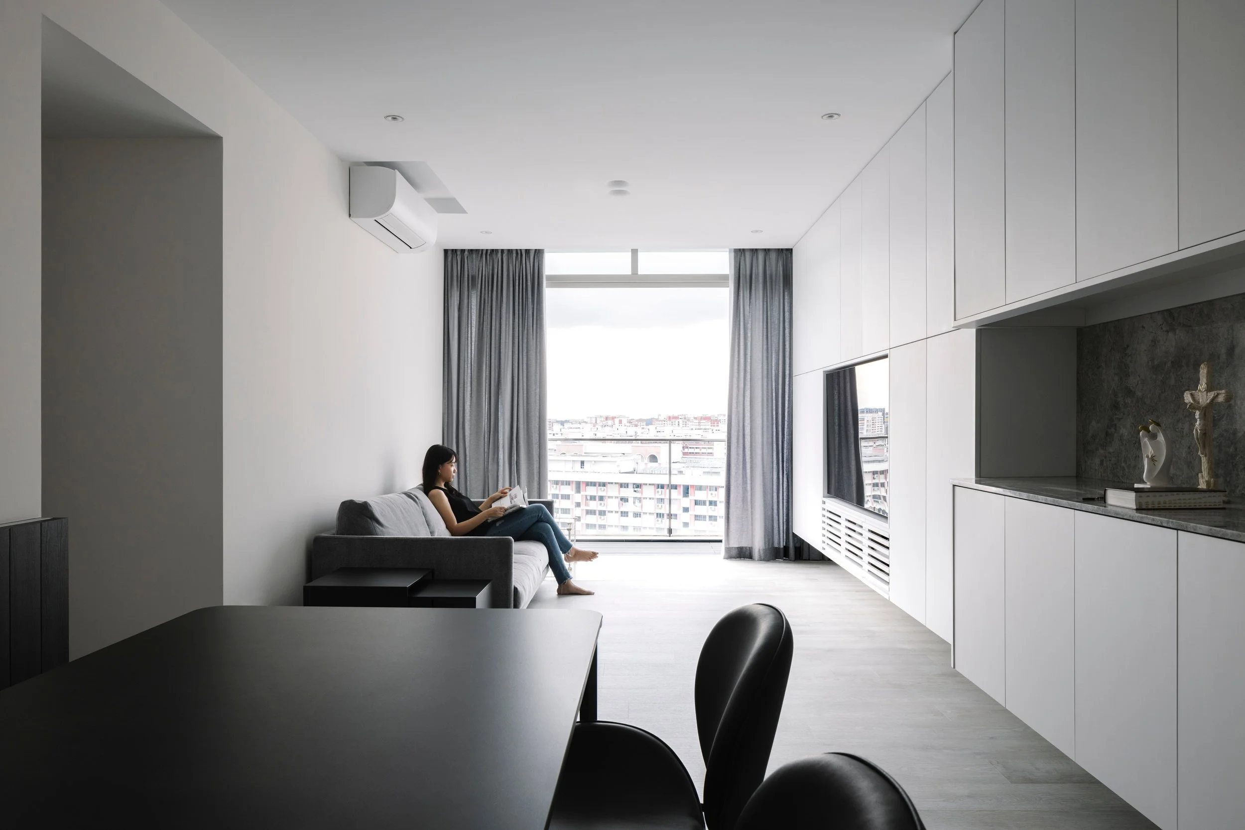 Bright minimalist condo living room in Singapore with full-height windows, built-in storage wall and grey interior palette, designed by Lite Design Collaborative.