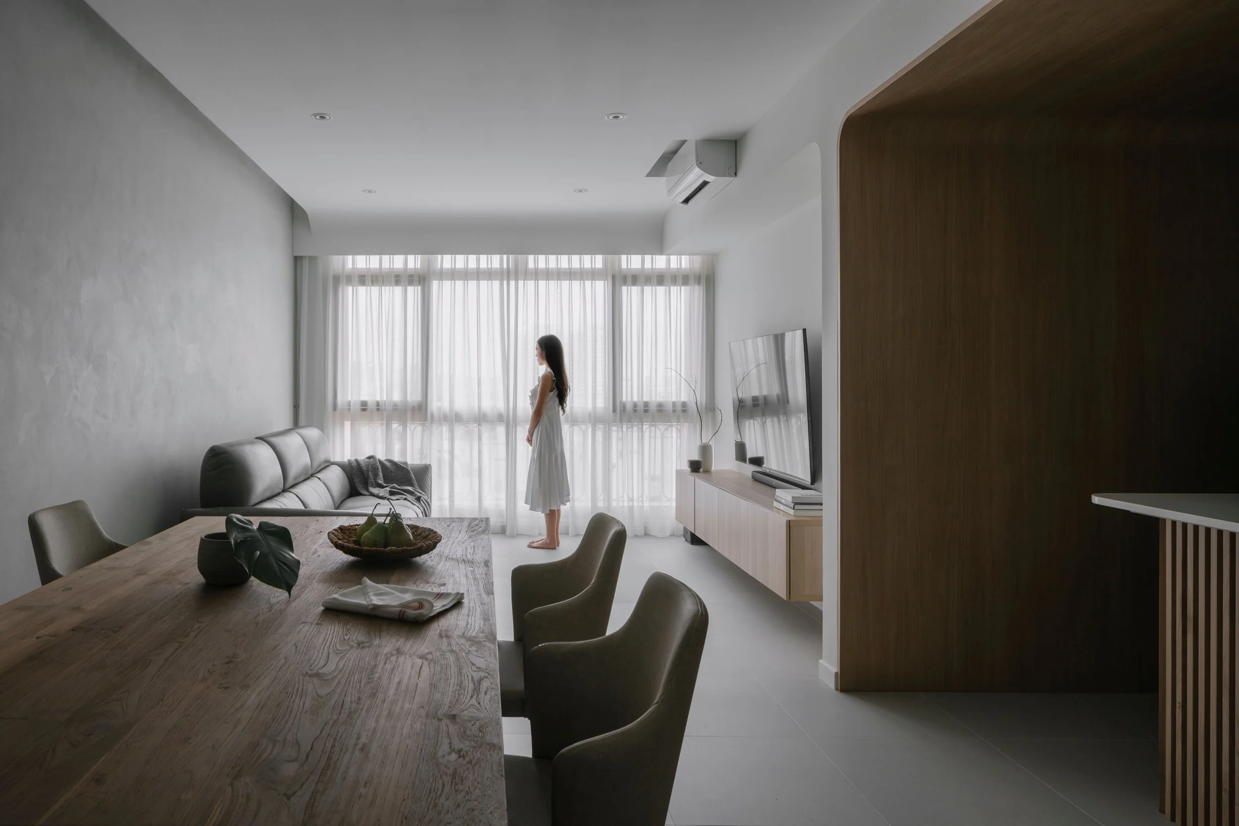 Open-concept living and dining space in Singapore with solid wood table, textured grey walls and soft natural lighting.