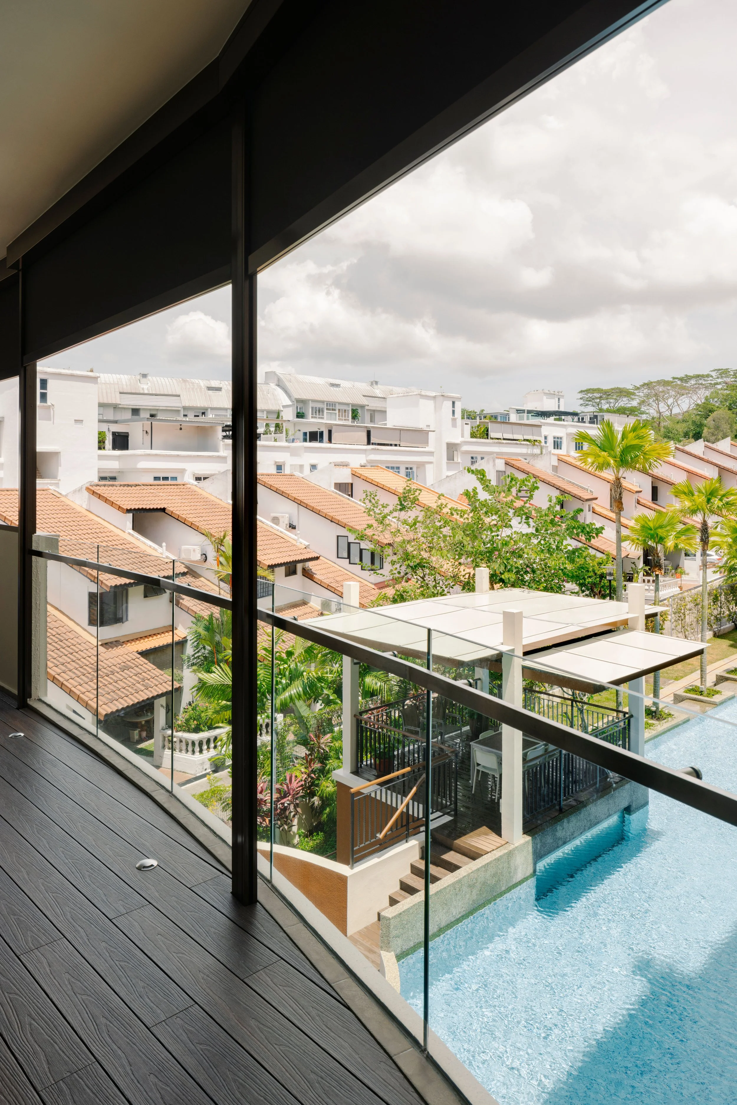 Modern condo balcony with glass railing and wood-look decking overlooking a pool and landed homes in Singapore.