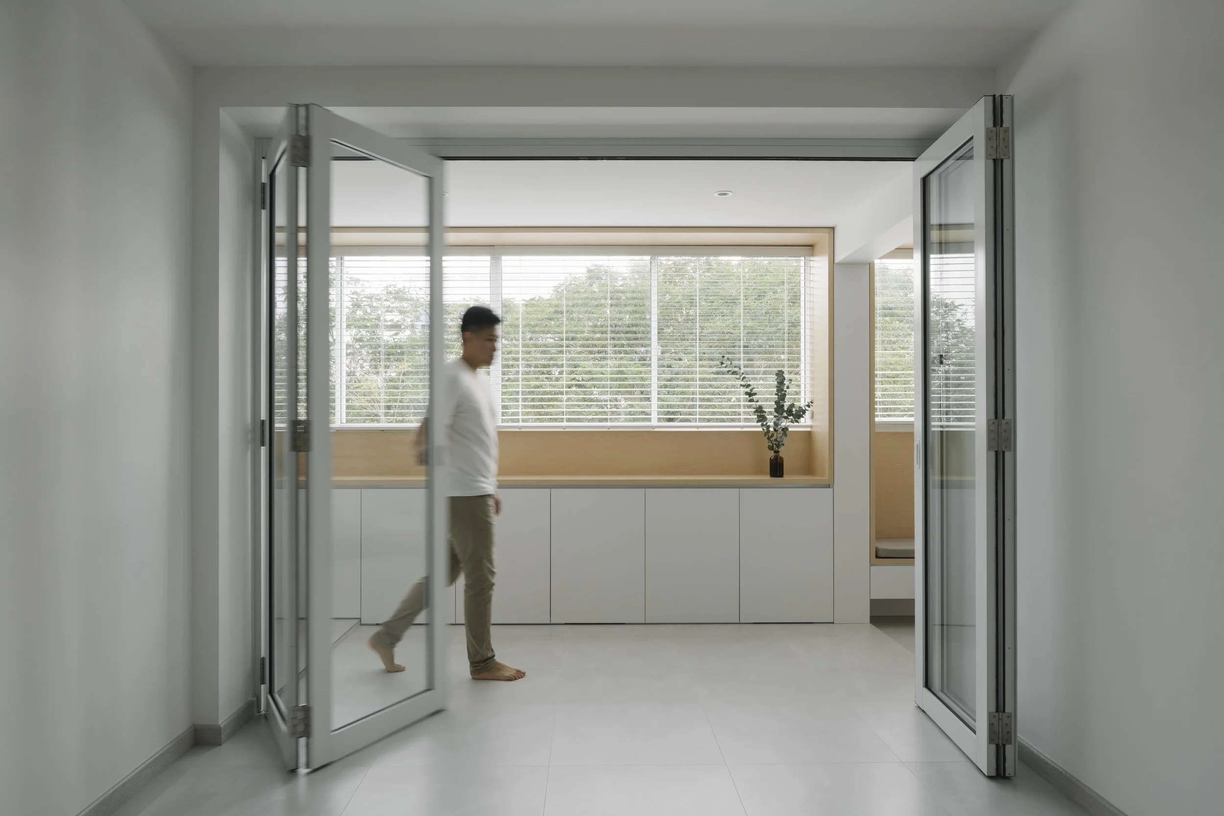 Aluminum bi-fold glass doors partially opened, revealing a bright minimalist interior with built-in cabinetry.