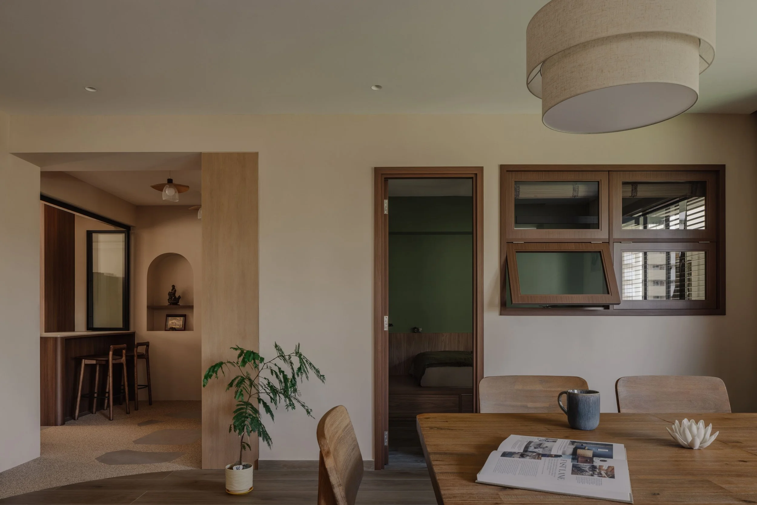 Warm modern dining area in a Singapore home featuring timber furniture, neutral walls and crafted window details, designed in a refined minimalist style.