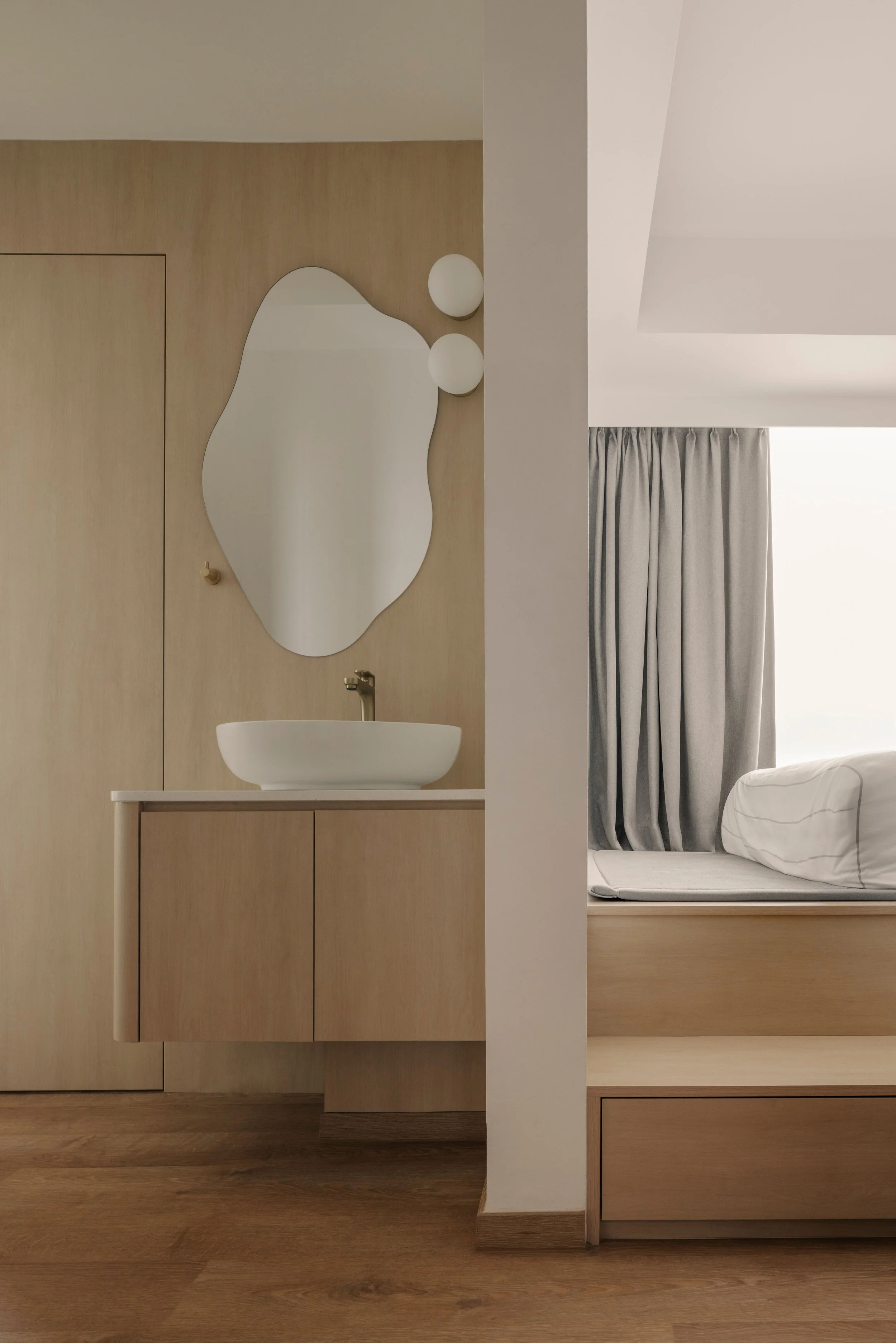 Modern minimalist vanity area with organic-shaped mirror, floating wood cabinet, and seamless transition to a cozy built-in bedroom platform.