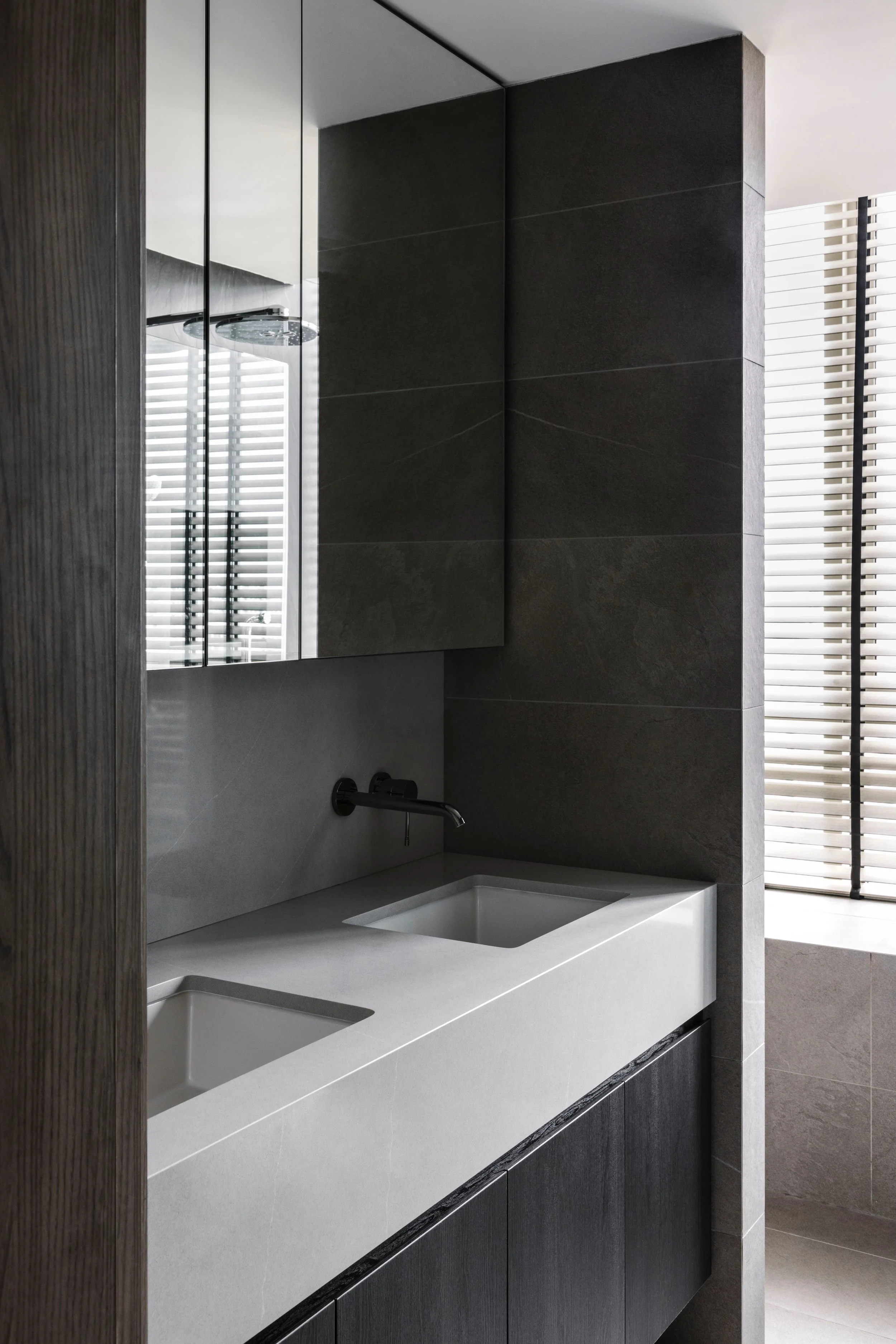 Modern bathroom with double integrated sinks, dark stone wall tiles and mirrored cabinets for a clean minimalist look.